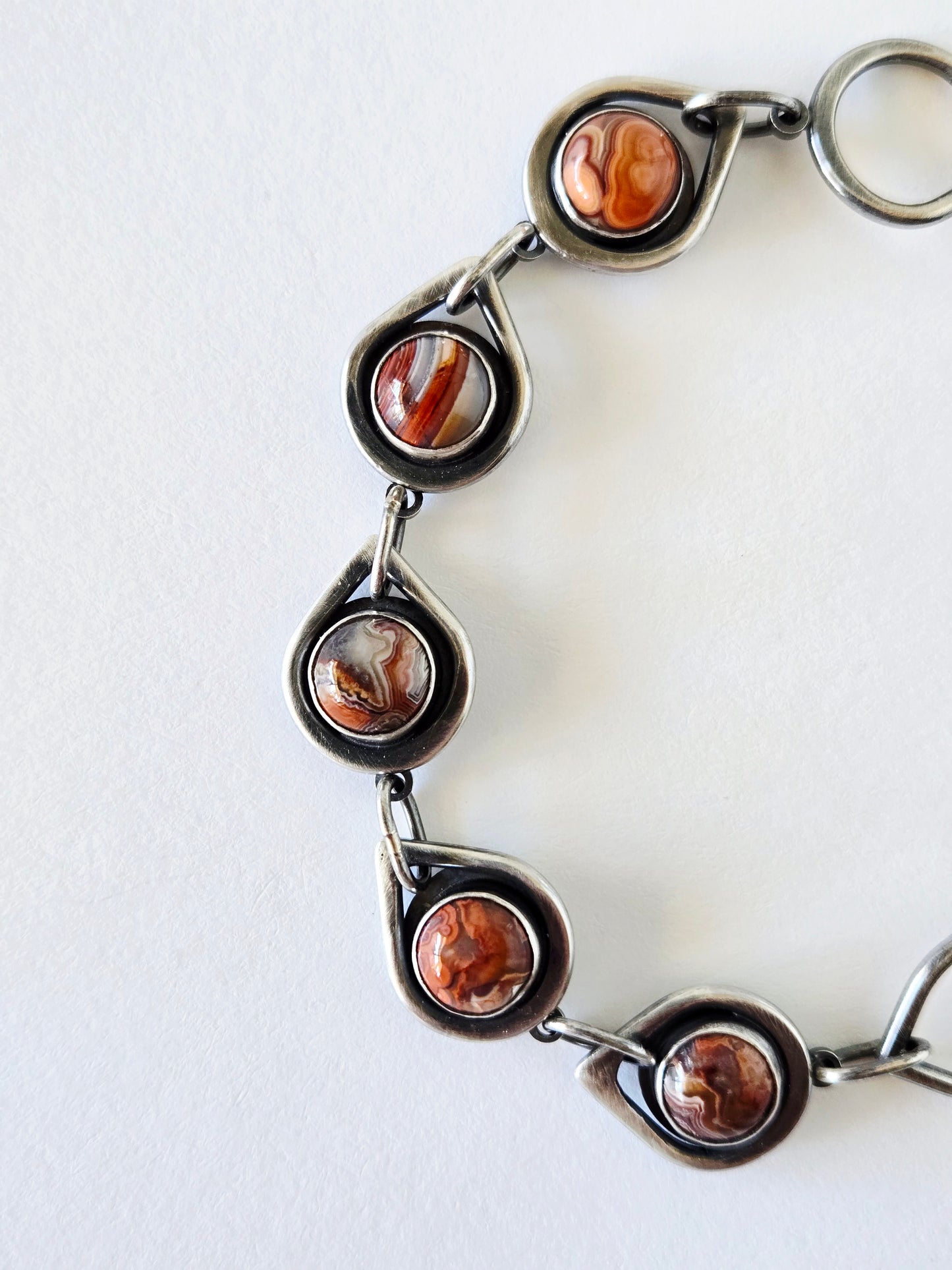 Silver bracelet with teardrop links and round red and orange agate detail on white background