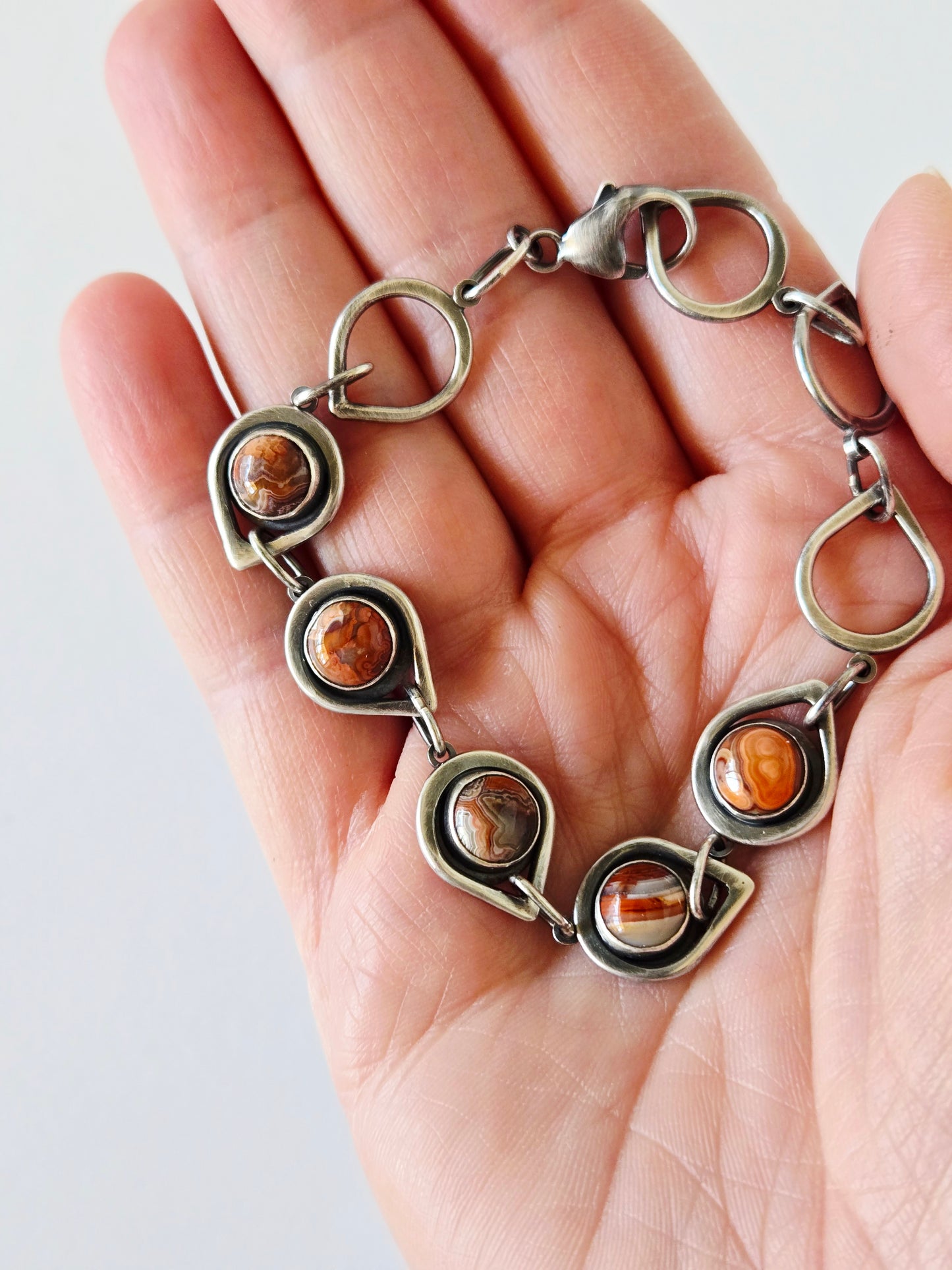 silver bracelet with multicolored agates held in a hand on a white background