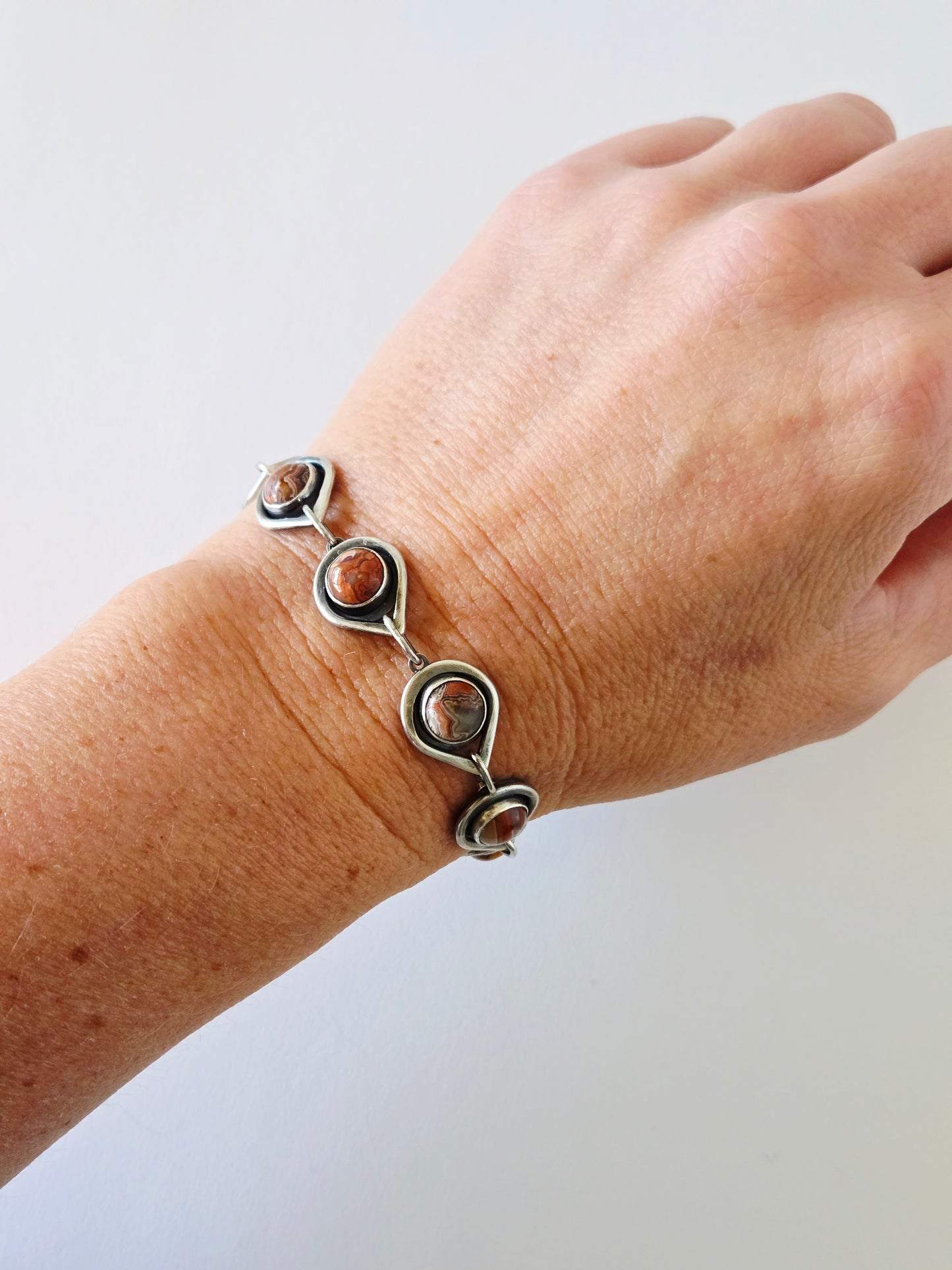 Silver bracelet with teardrop links and round stones on a wrist against a light background