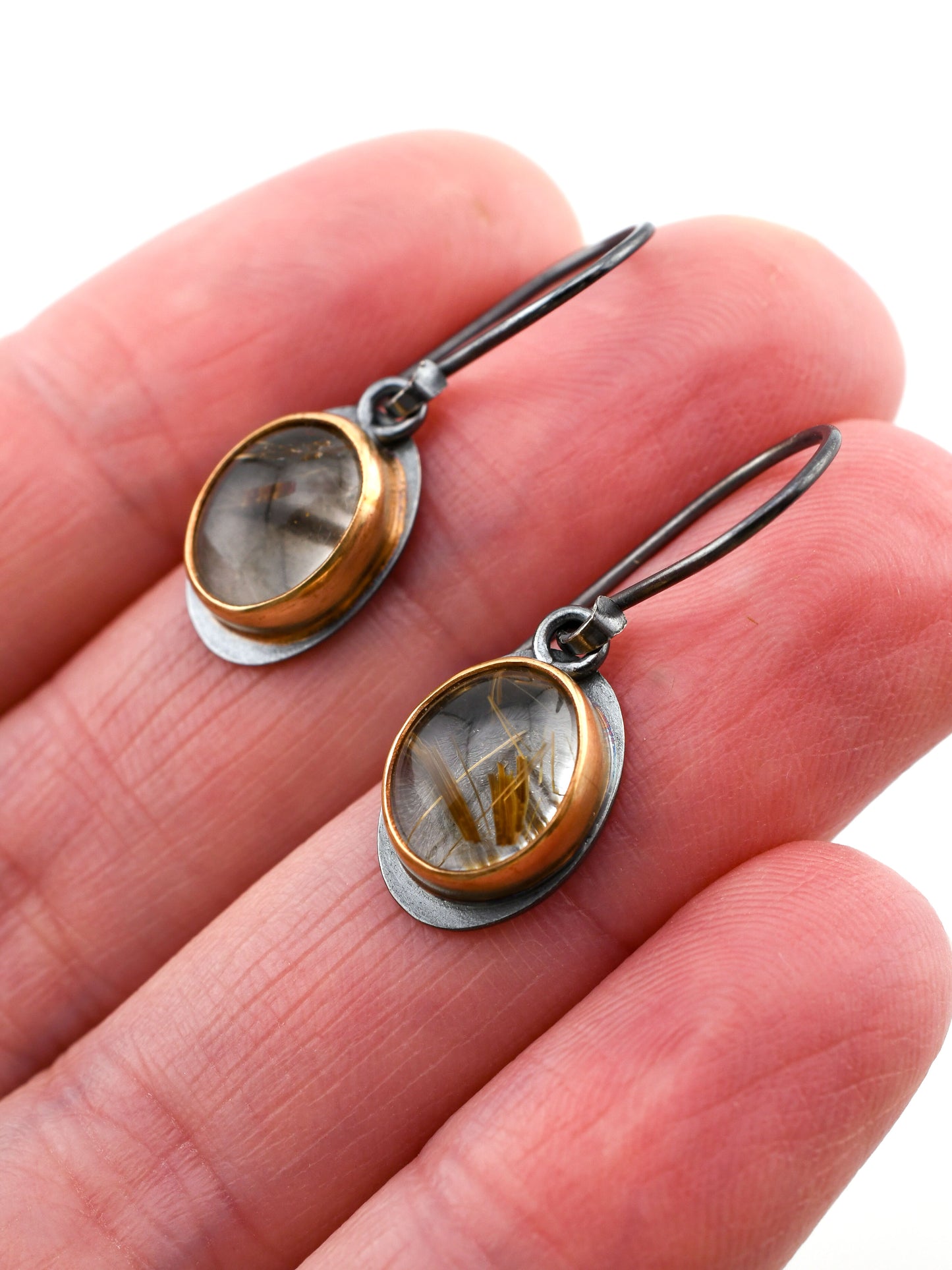 Pair of earrings with gold and silver design held between fingers on a white background