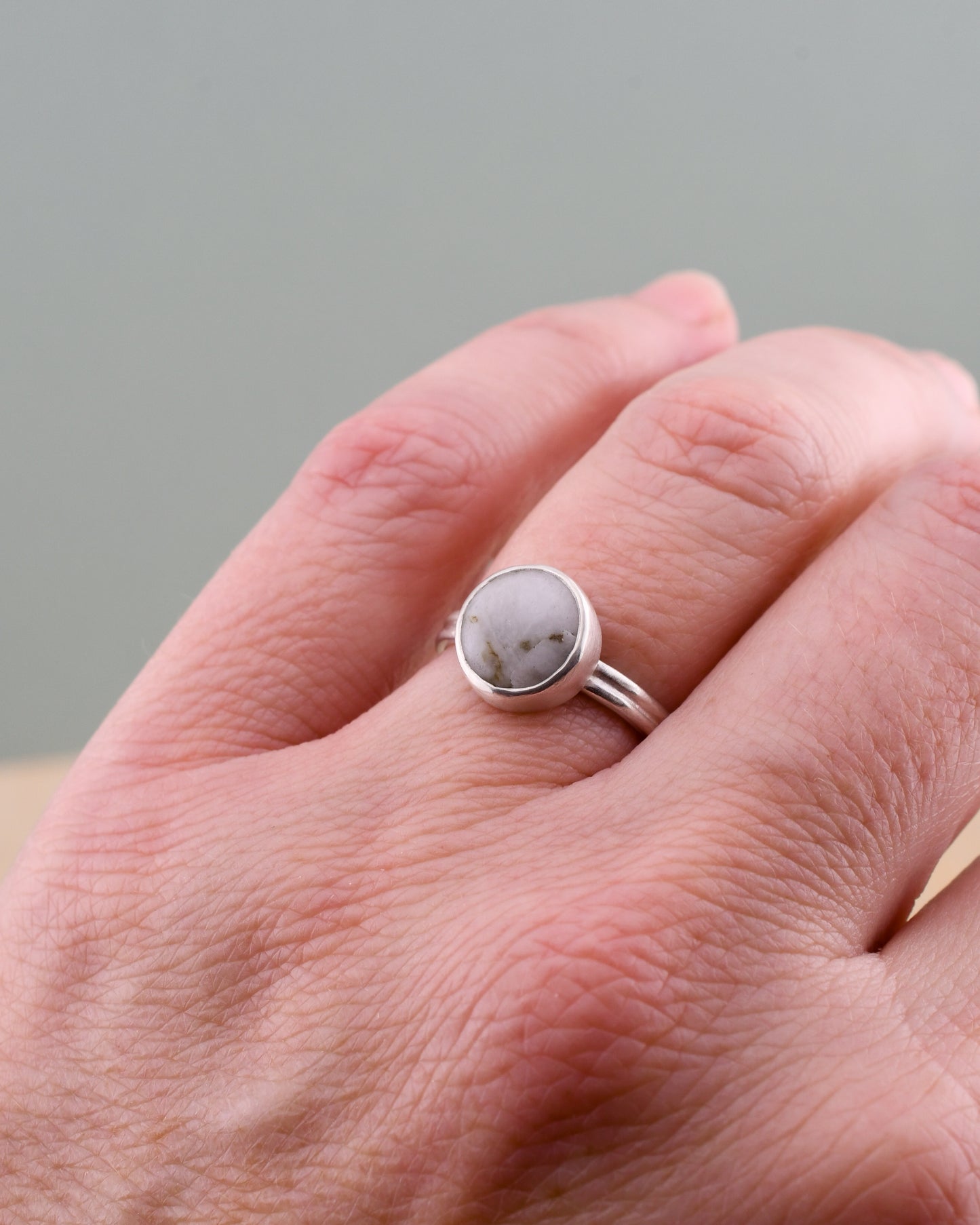Silver ring with a round white beach stone on a hand against a gray background