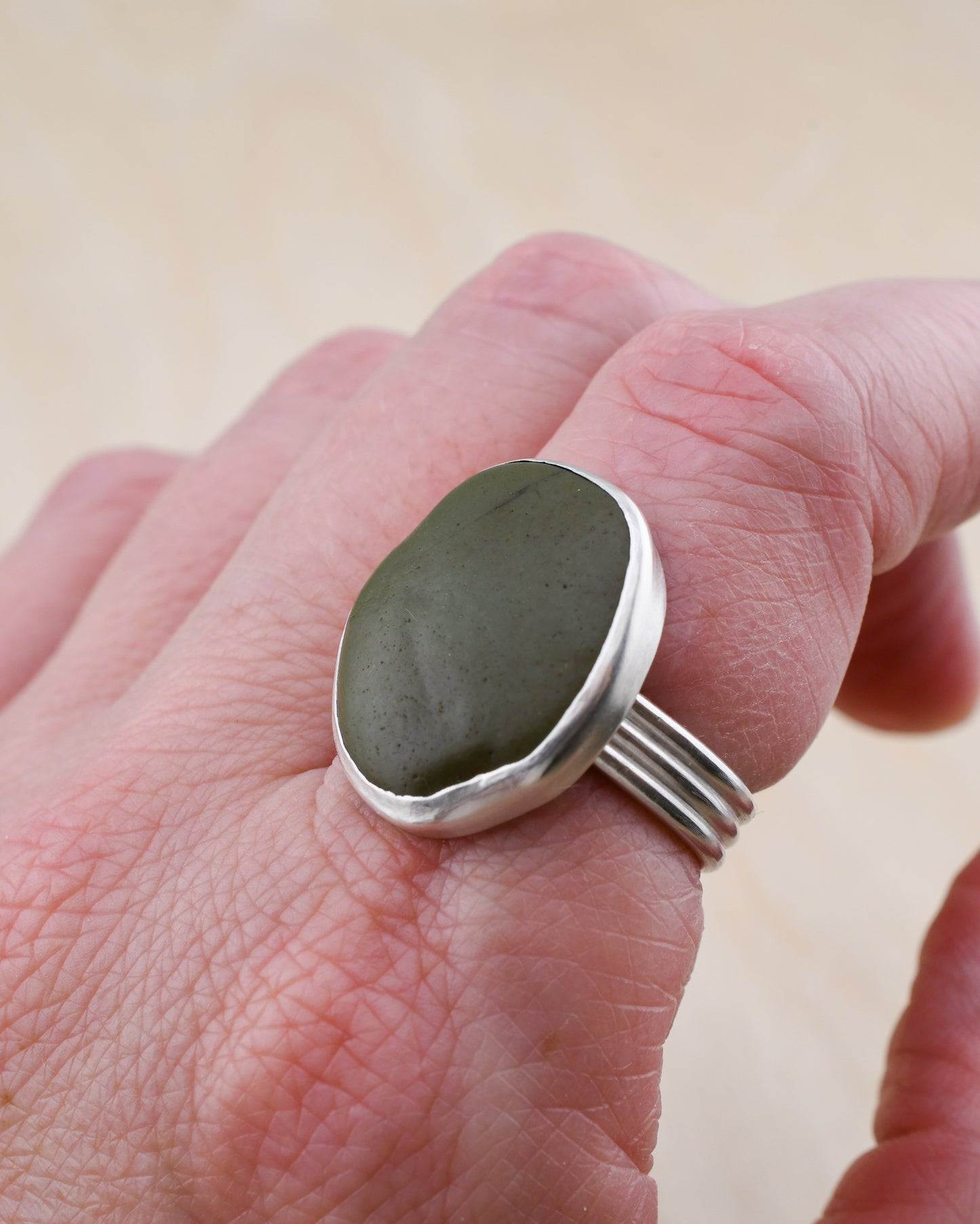 Hand wearing a silver ring with a green stone on a plain background