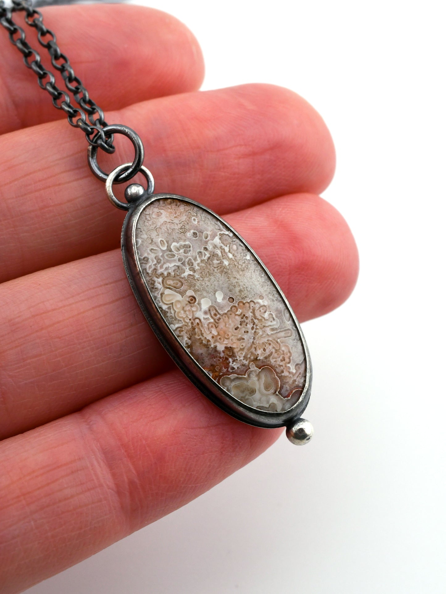 Necklace with an oval pendant held between fingers on a white background