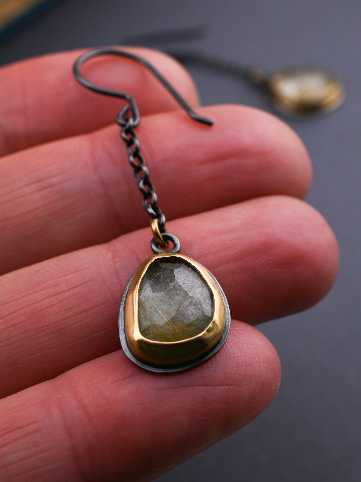 Gold and silver pendant held between fingers with a dark background