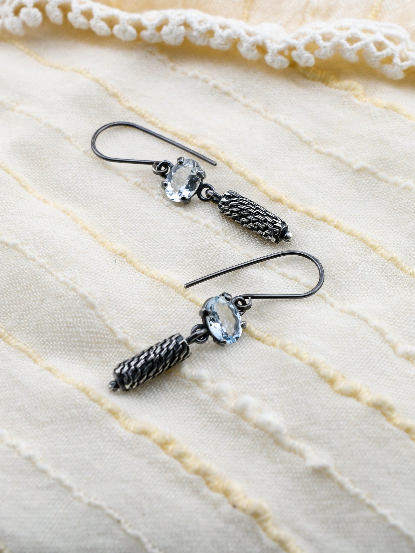 Pair of earrings with black and silver design on a textured beige fabric background