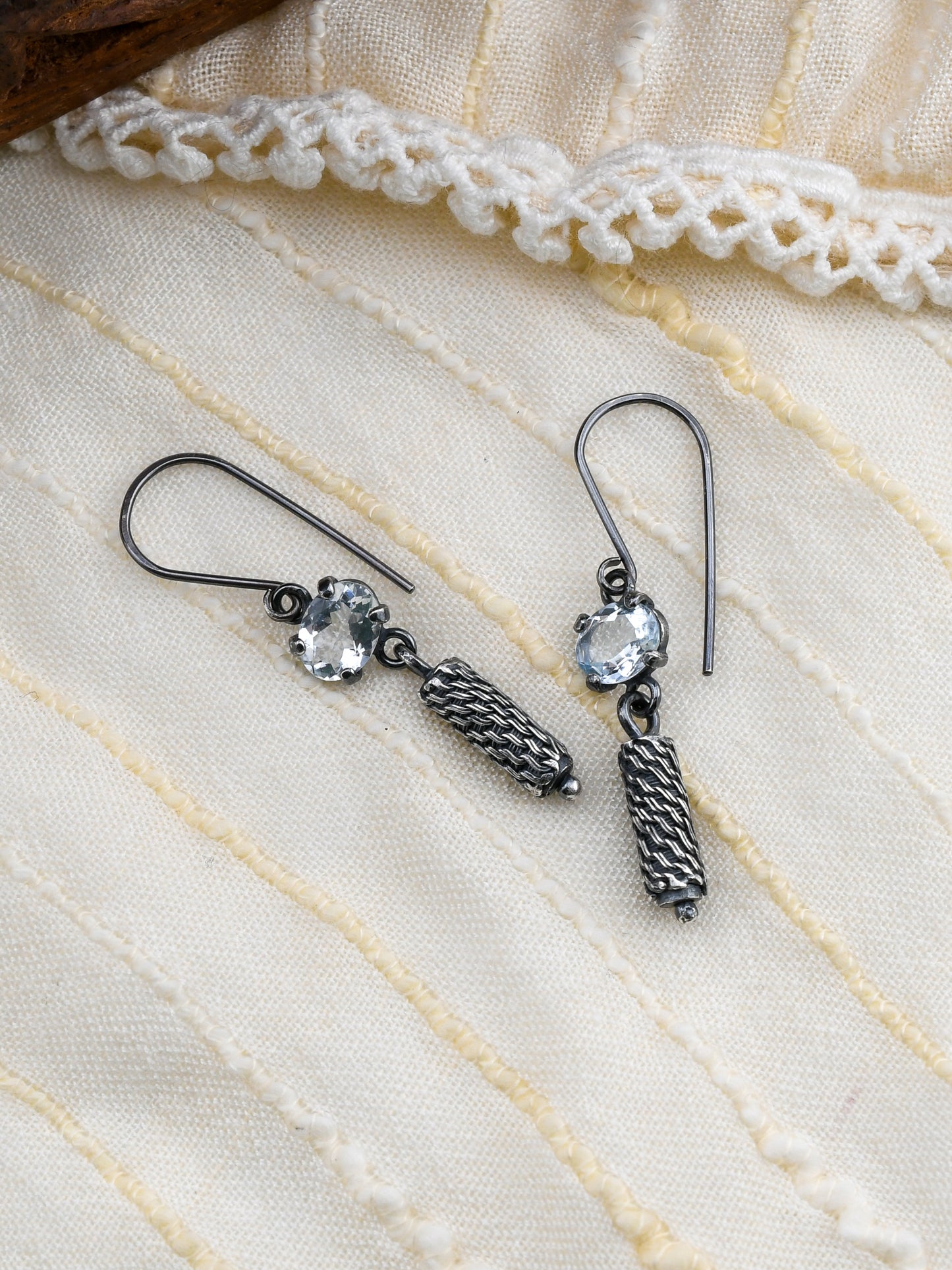 Silver earrings with pale blue gemstones on a textured white fabric background
