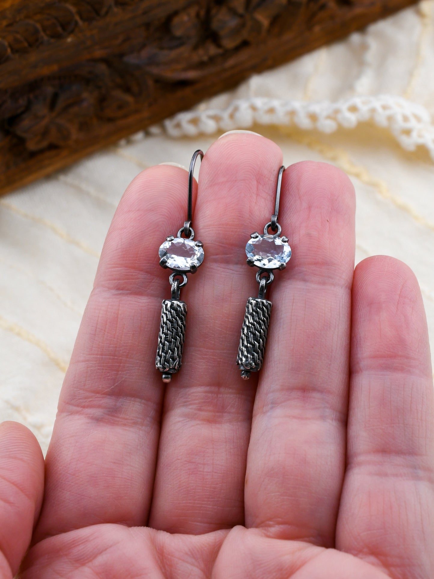 Silver earrings with gemstones held between fingers on a textured surface