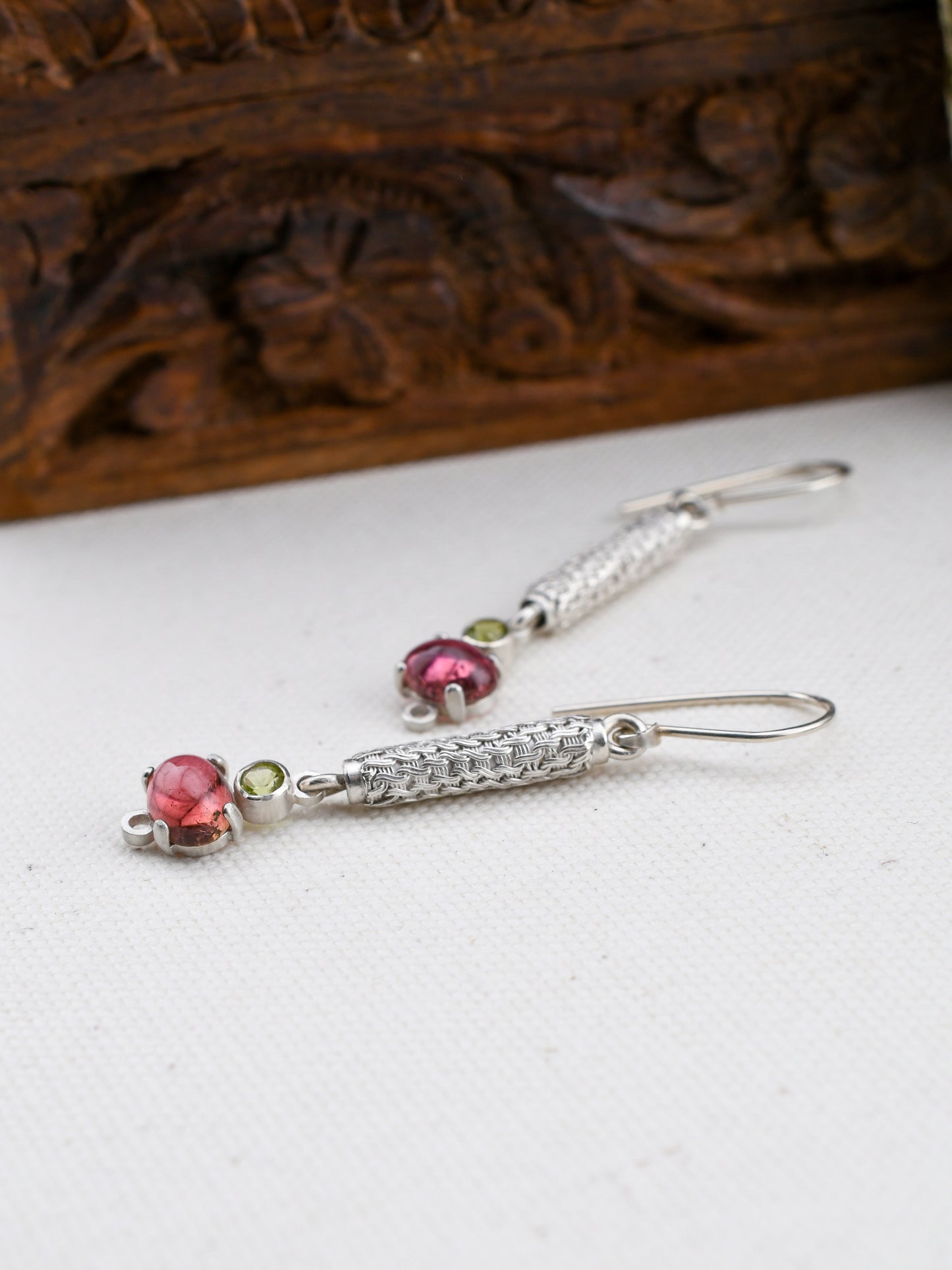 Silver earrings with gemstones on a white surface with a wooden box in the background