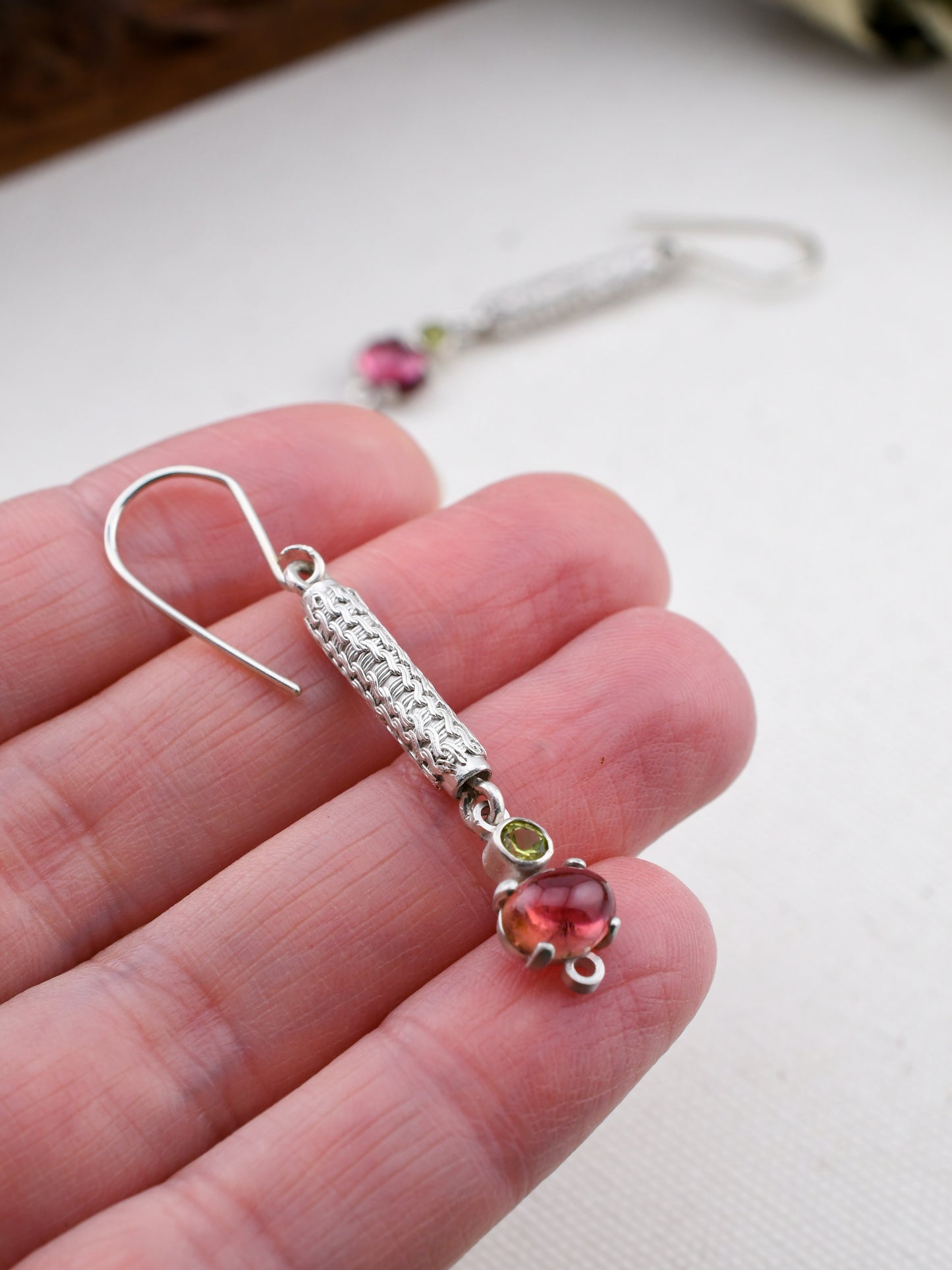 Silver earring with a pink gemstone held between fingers on a white background