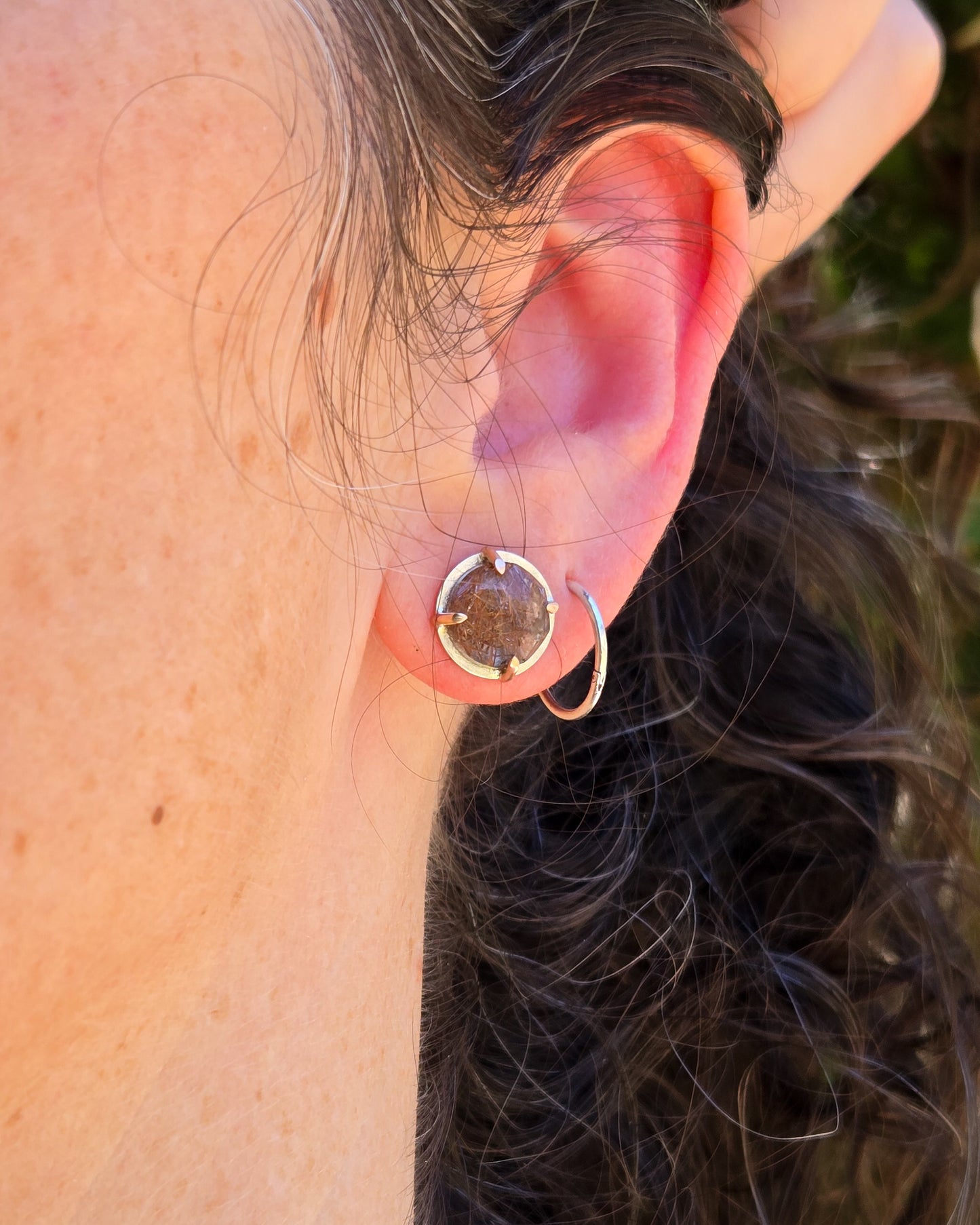 rutilated quartz stud earrings in silver and rose gold shown worn on an ear in natural light