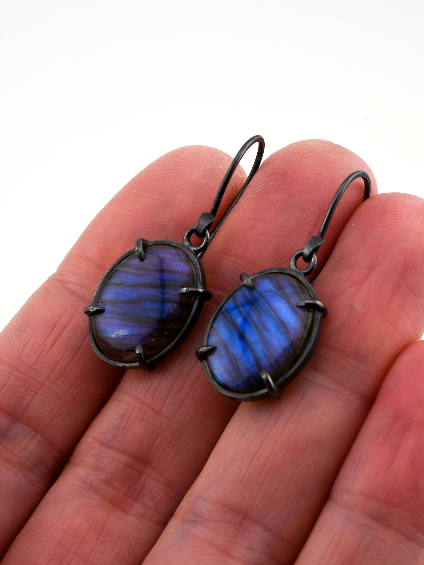 Blue stone earrings held in a hand on a white background
