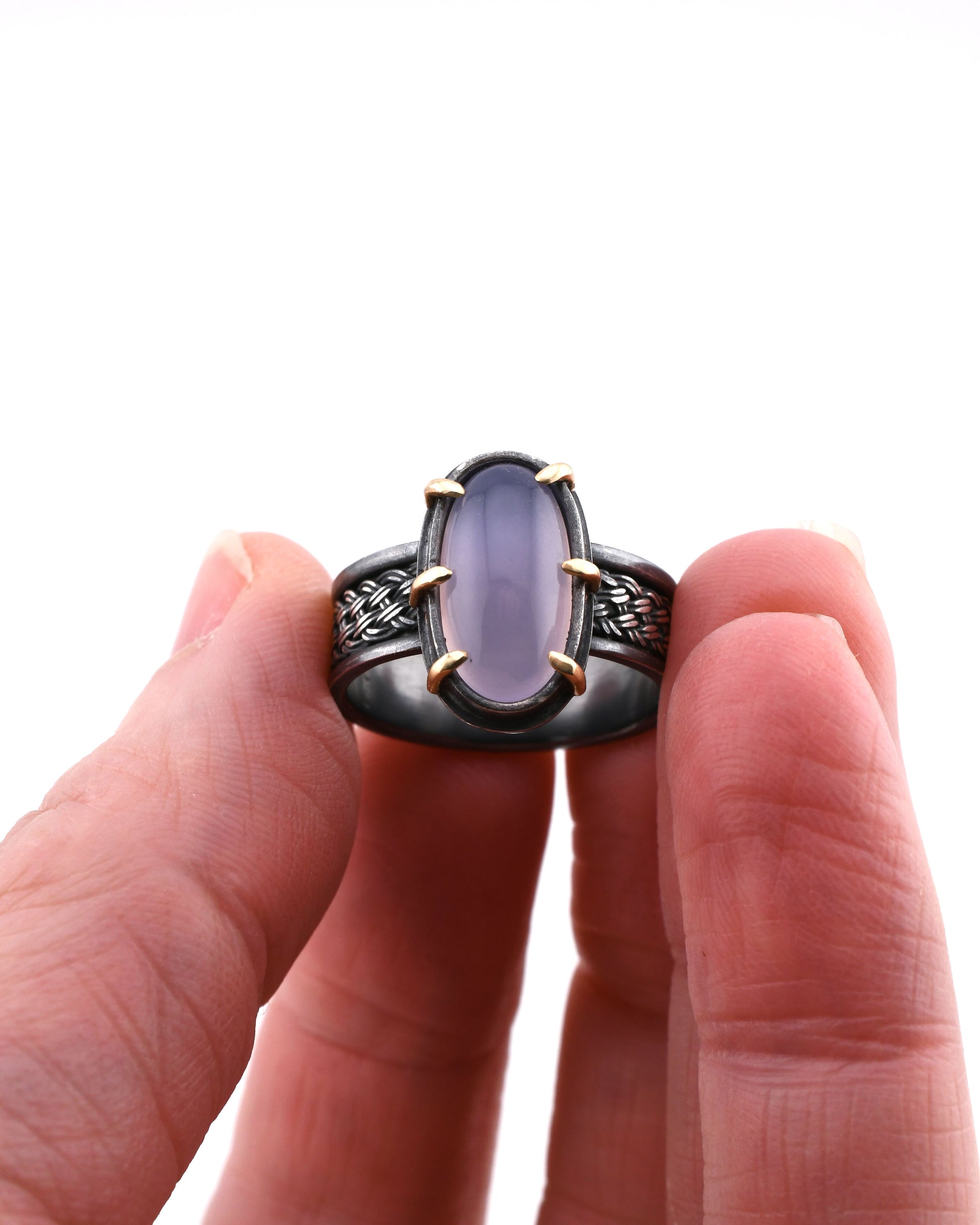 Hand holding a ring with a purple stone against a white background
