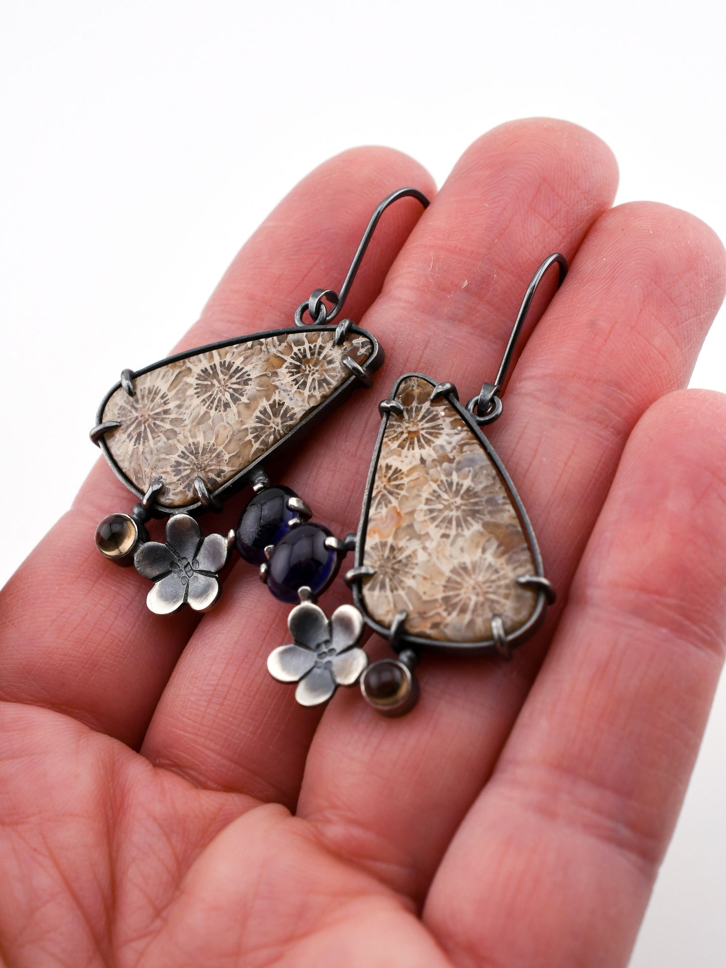 Hand holding a pair of floral-themed earrings with natural elements.