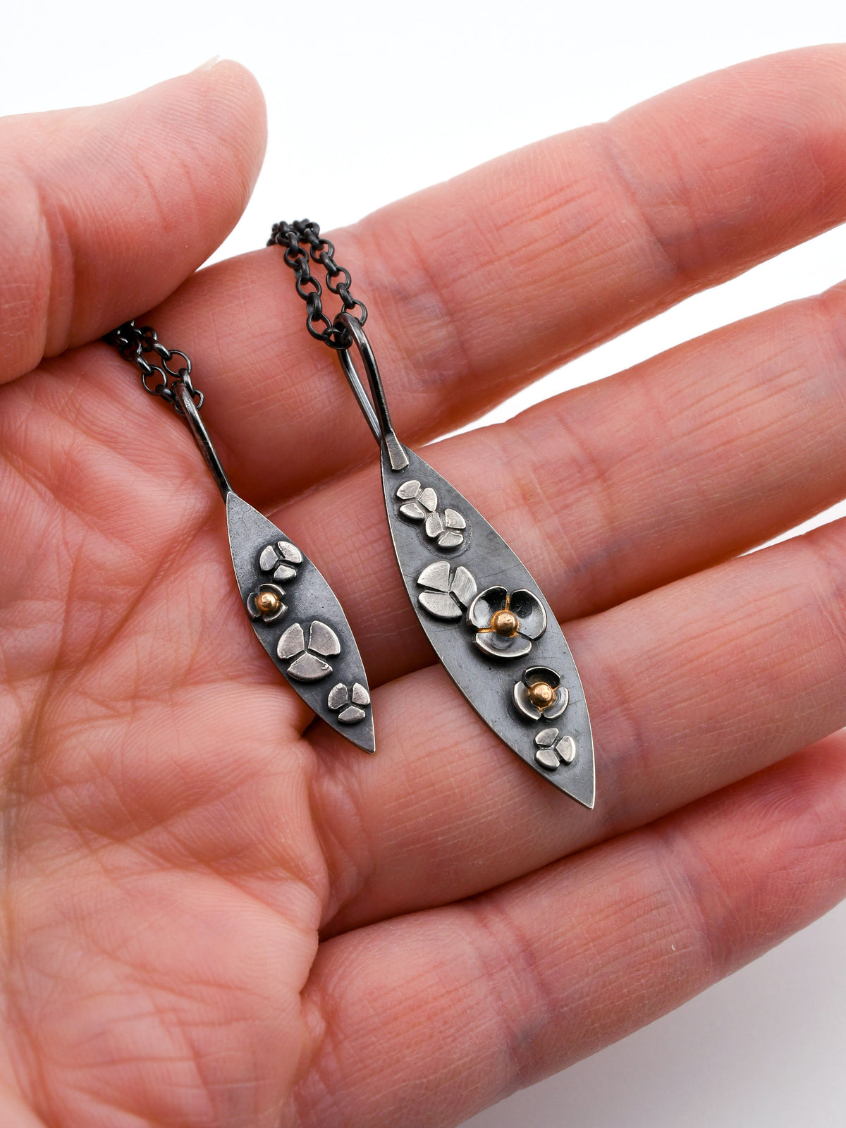 A hand holding two different sized pendants in the Garland design, showing the petite and regular size over a white background