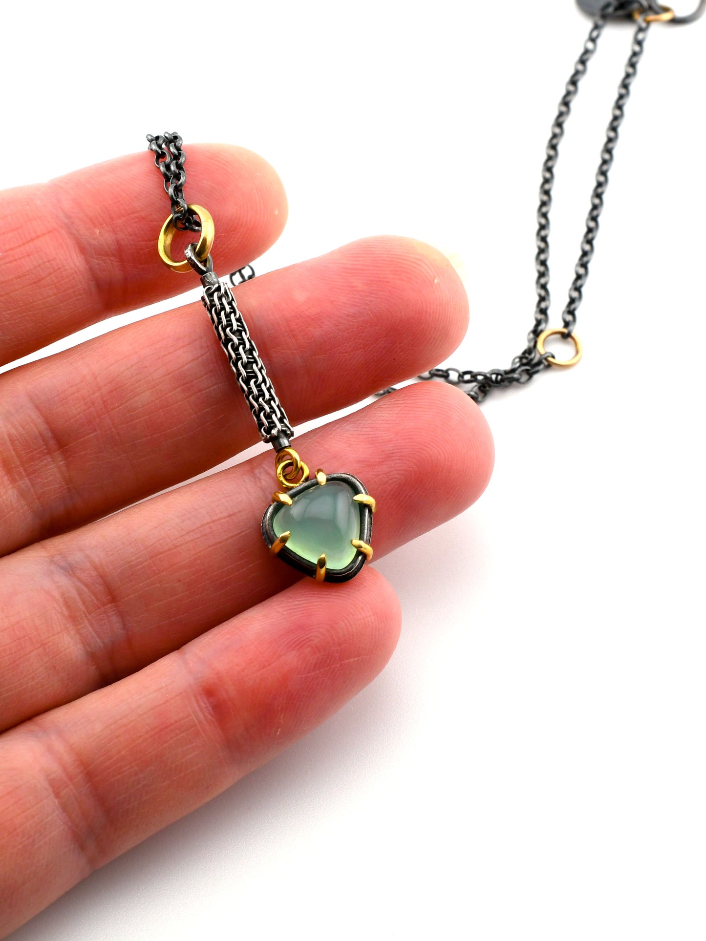Necklace with a green gemstone pendant held between fingers on a white background