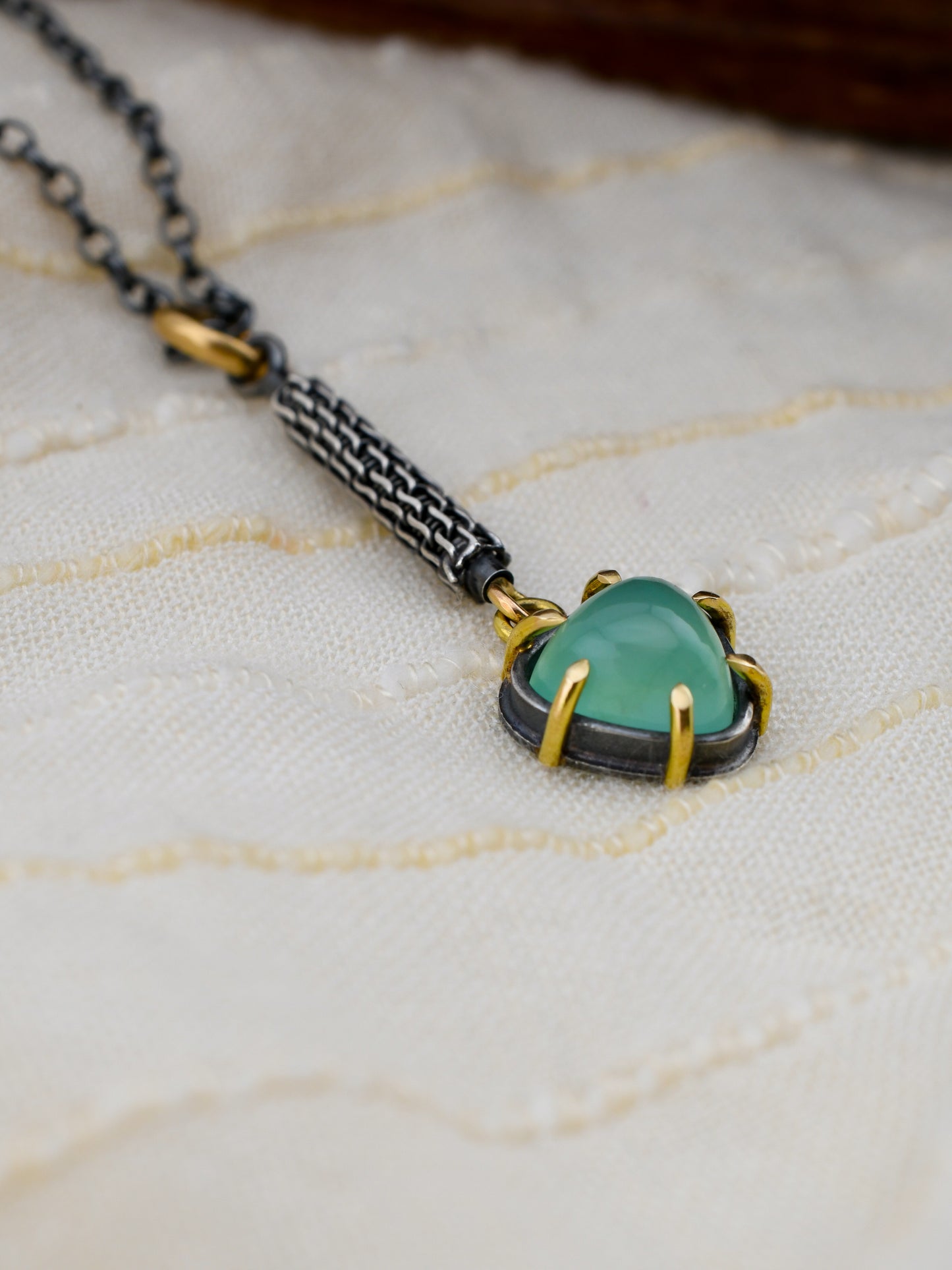 Necklace with a green gemstone pendant on a textured fabric background
