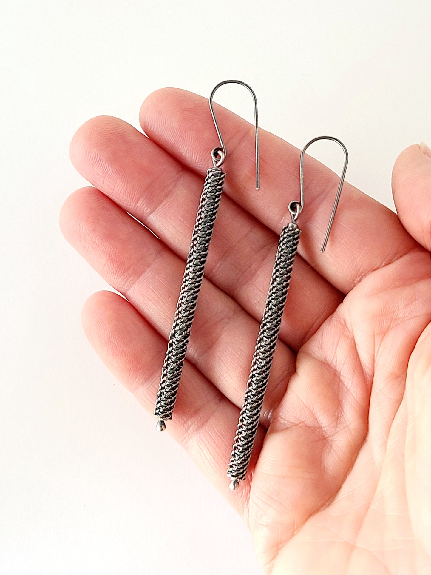 Silver rope-style earrings held in a hand against a white background