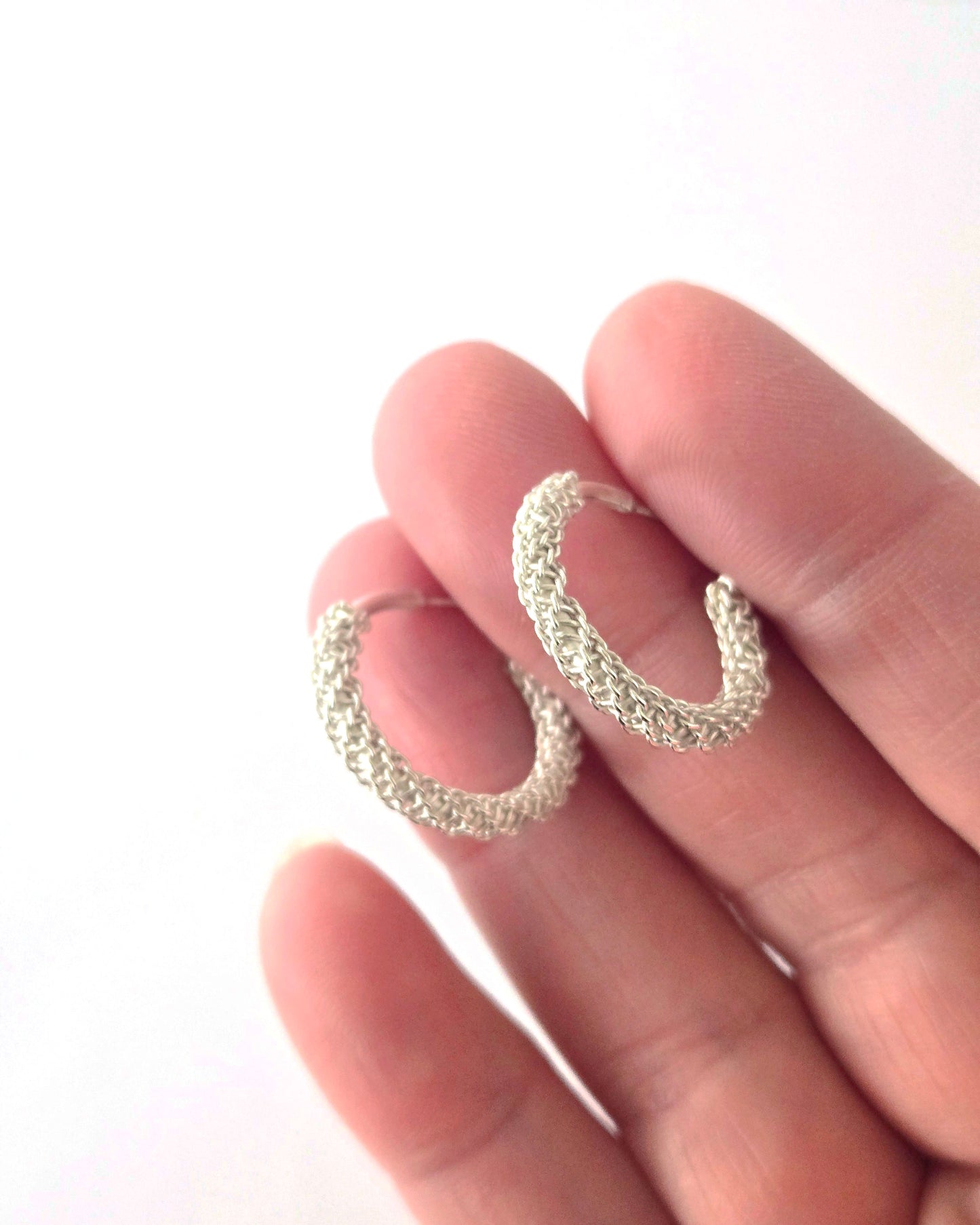 Silver hoop earrings held between fingers on a white background