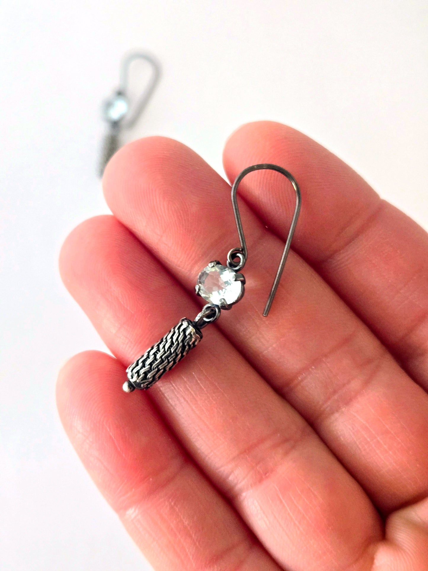 Silver earring with a ice blue gemstone held between fingers on a white background