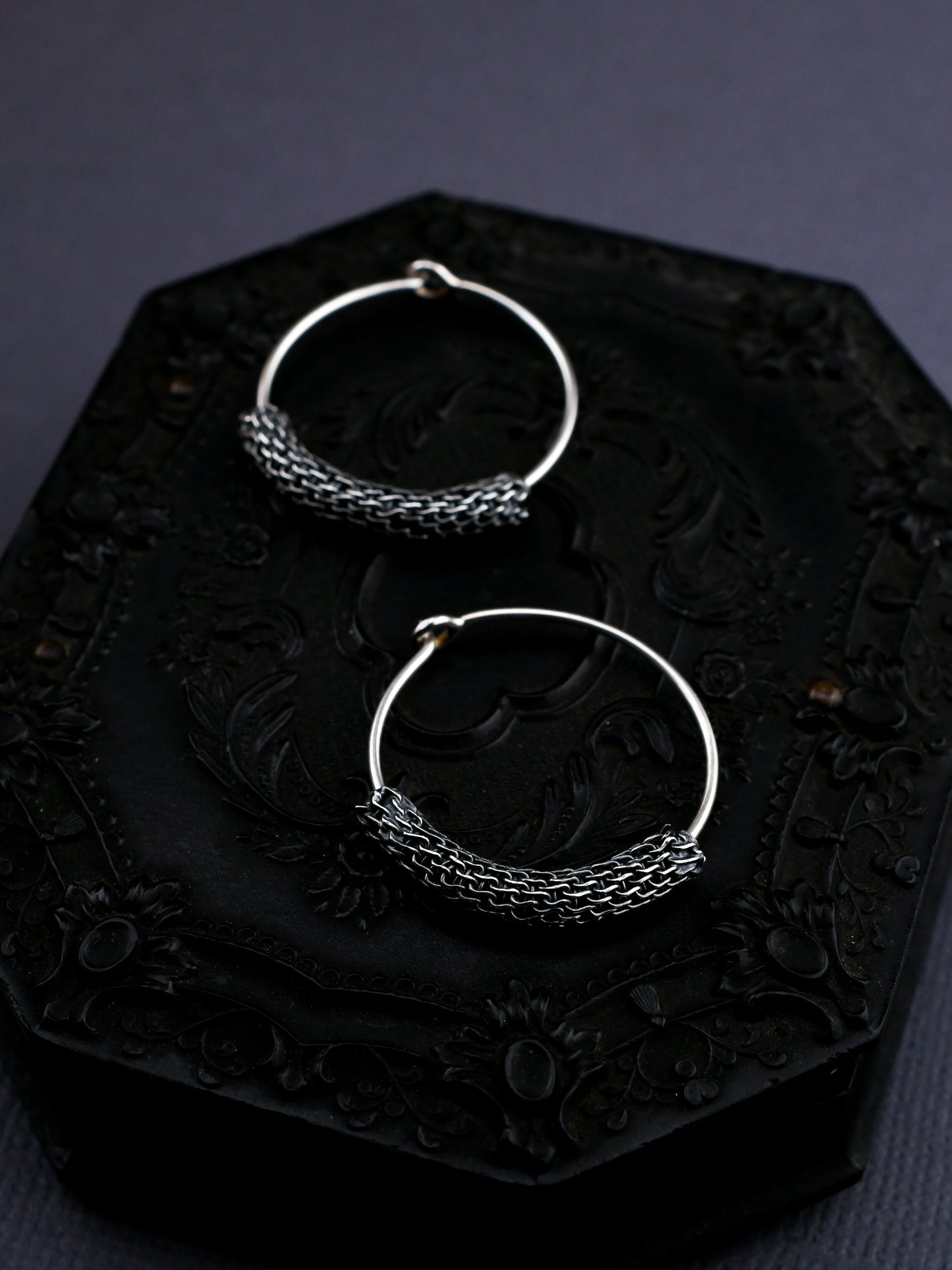 Two silver hoop earrings on a dark textured surface