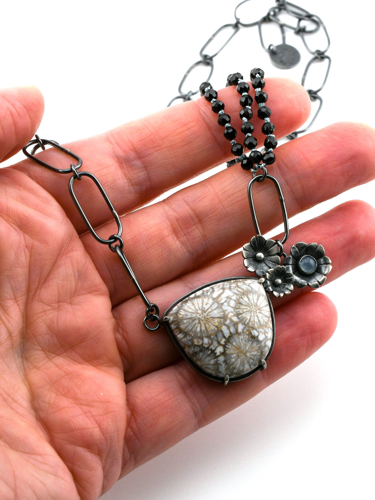 Necklace with floral pendant held in a hand against a white background