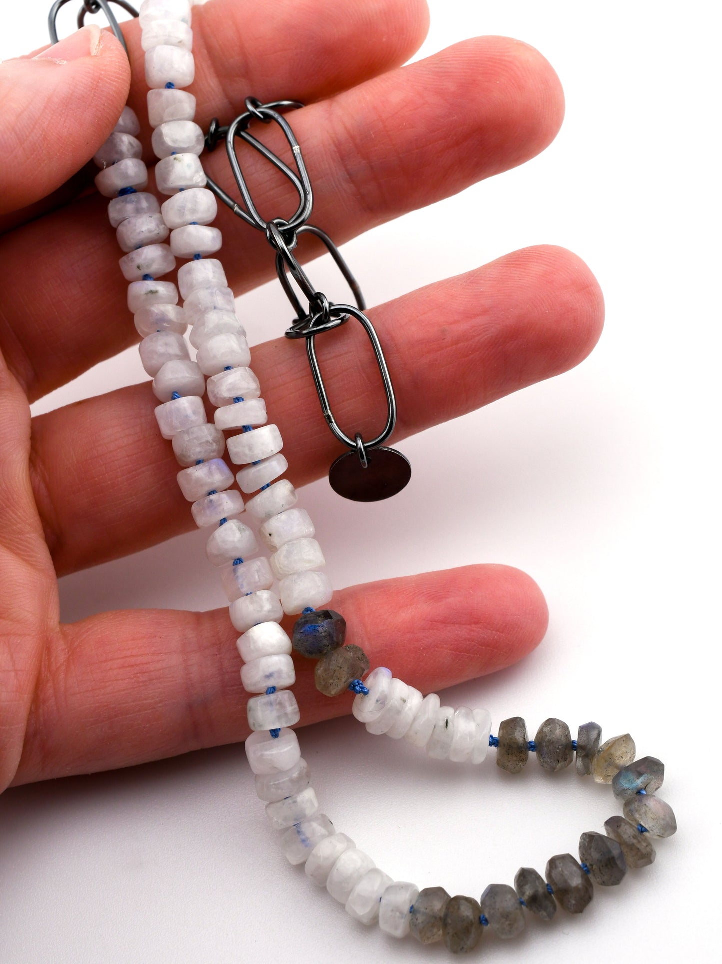 hand holding a moonstone and labradorite beaded necklace on a white background