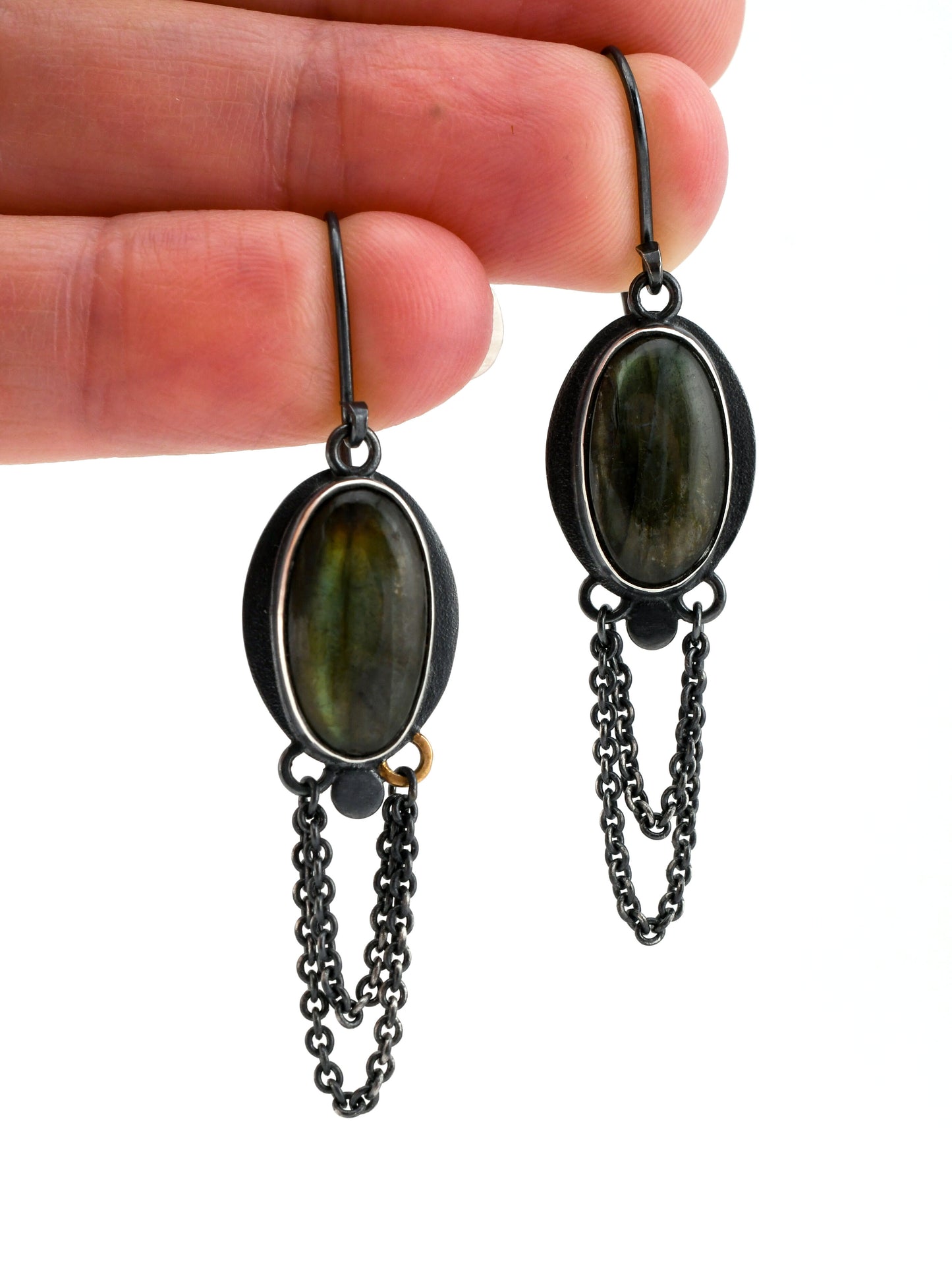 Pair of earrings with green stones and chain details held between fingers on a white background