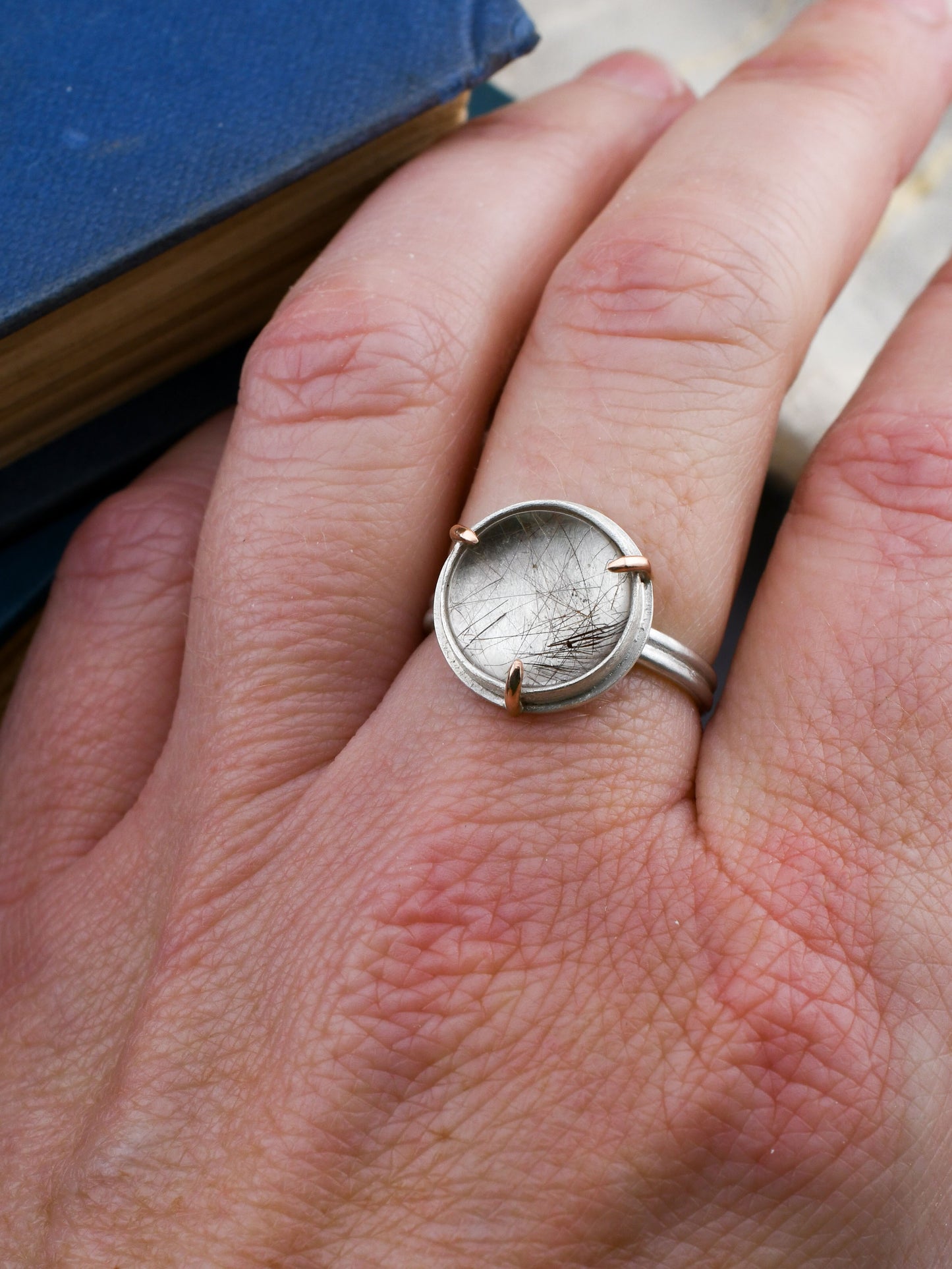 Silver ring with a round rutilated quartz on a person's finger