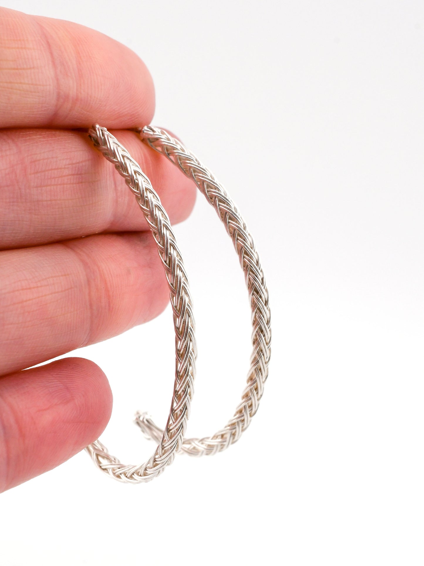 Silver braided hoop earrings held between fingers against a white background