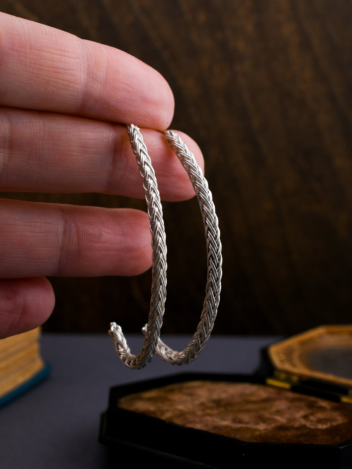 Hand holding braided silver hoop earrings against a dark background