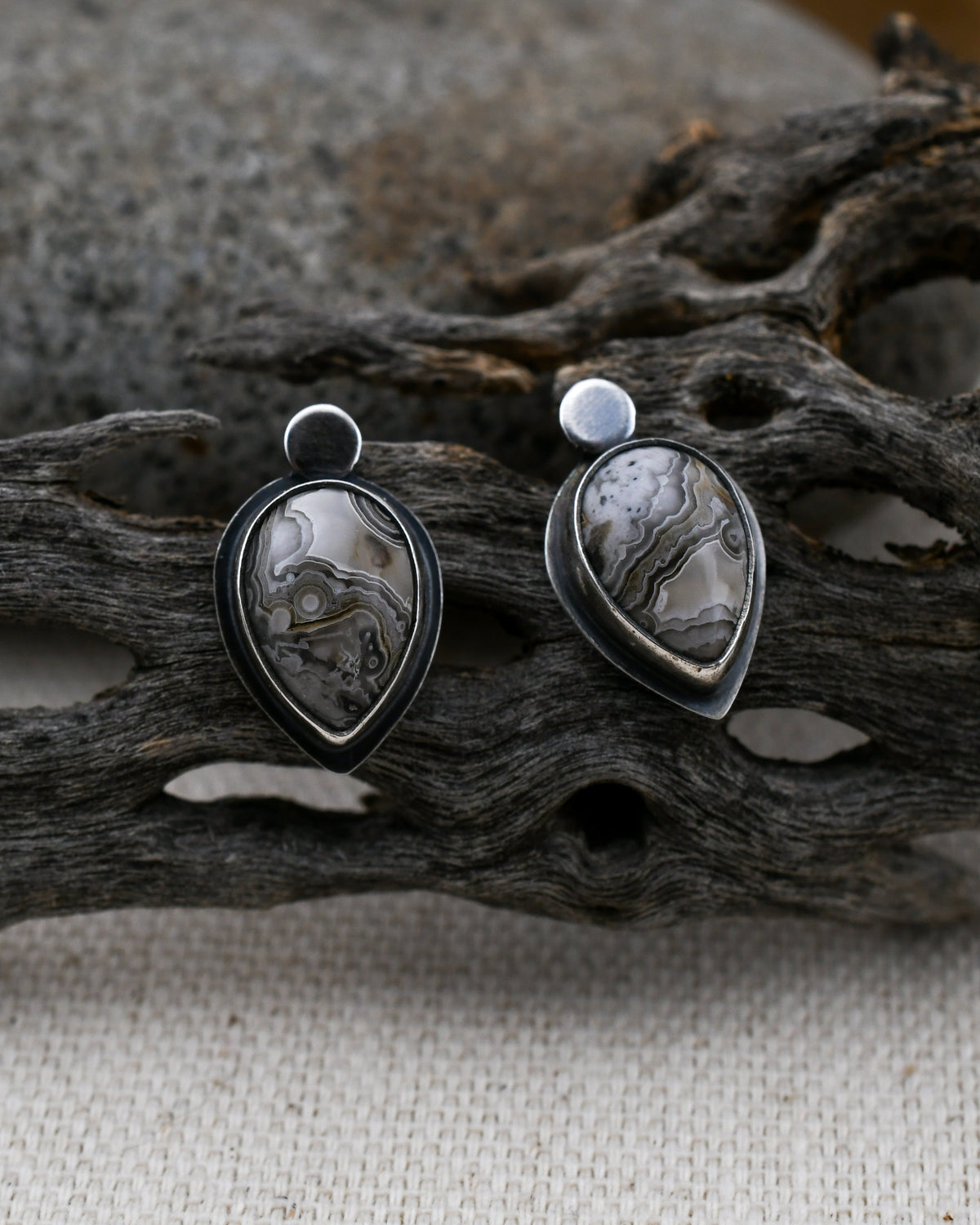 Sterling silver teardrop stud earrings with gray and cream crazy lace agate displayed on cactus wood and linen