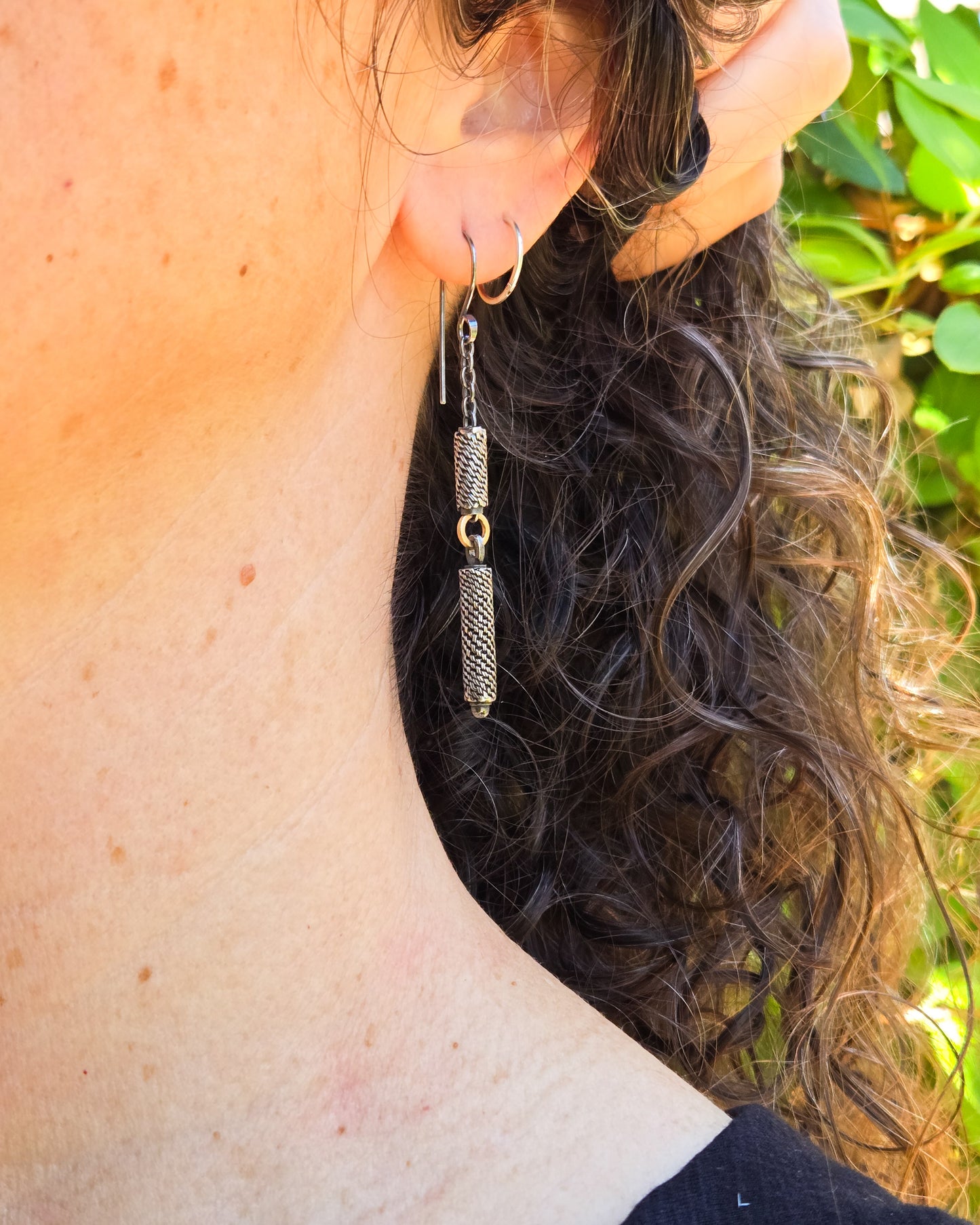 Close-up of a person wearing a woven silver earring with a blurred natural background
