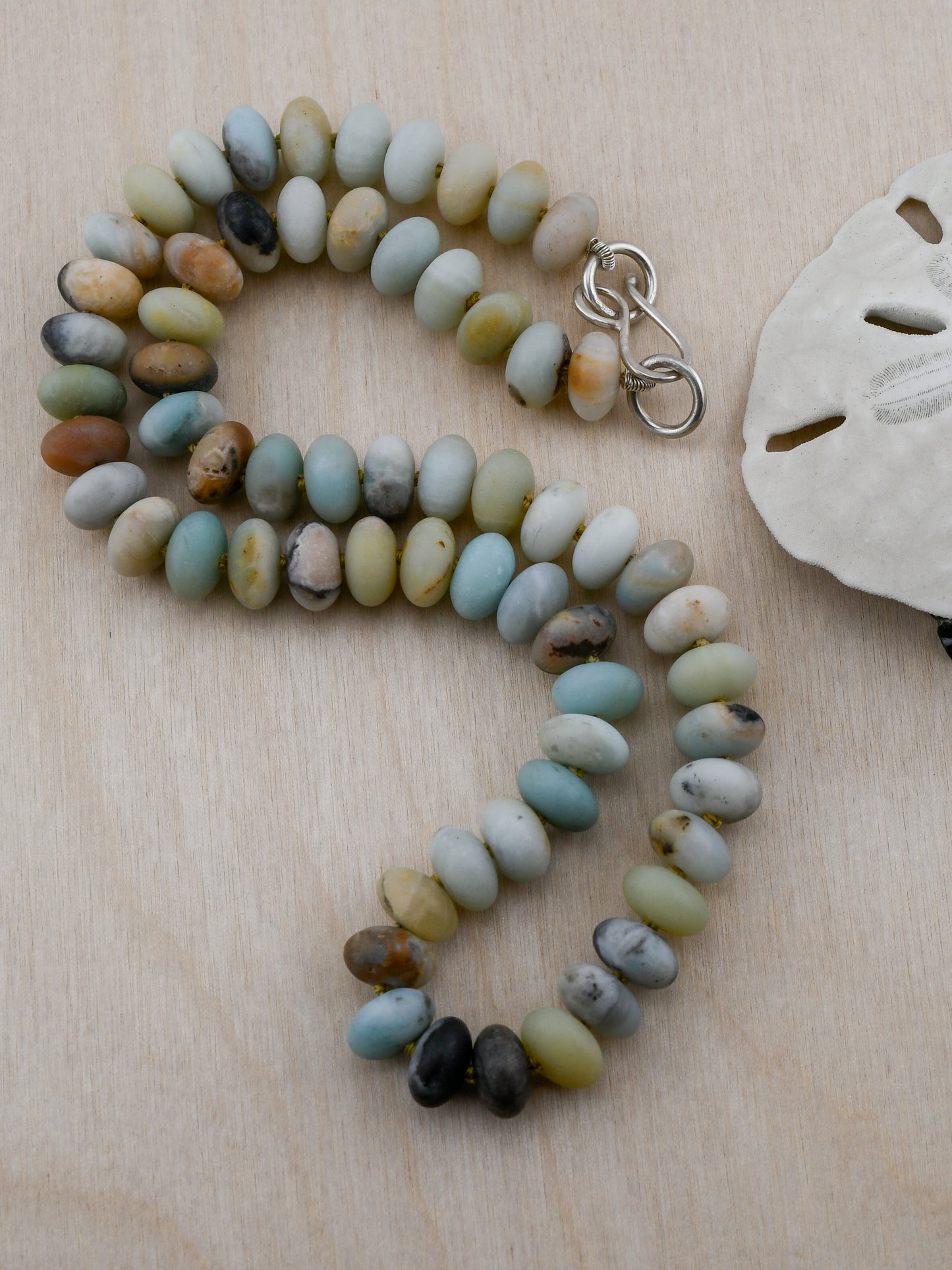 Beaded necklace on a wooden surface with a sand dollar