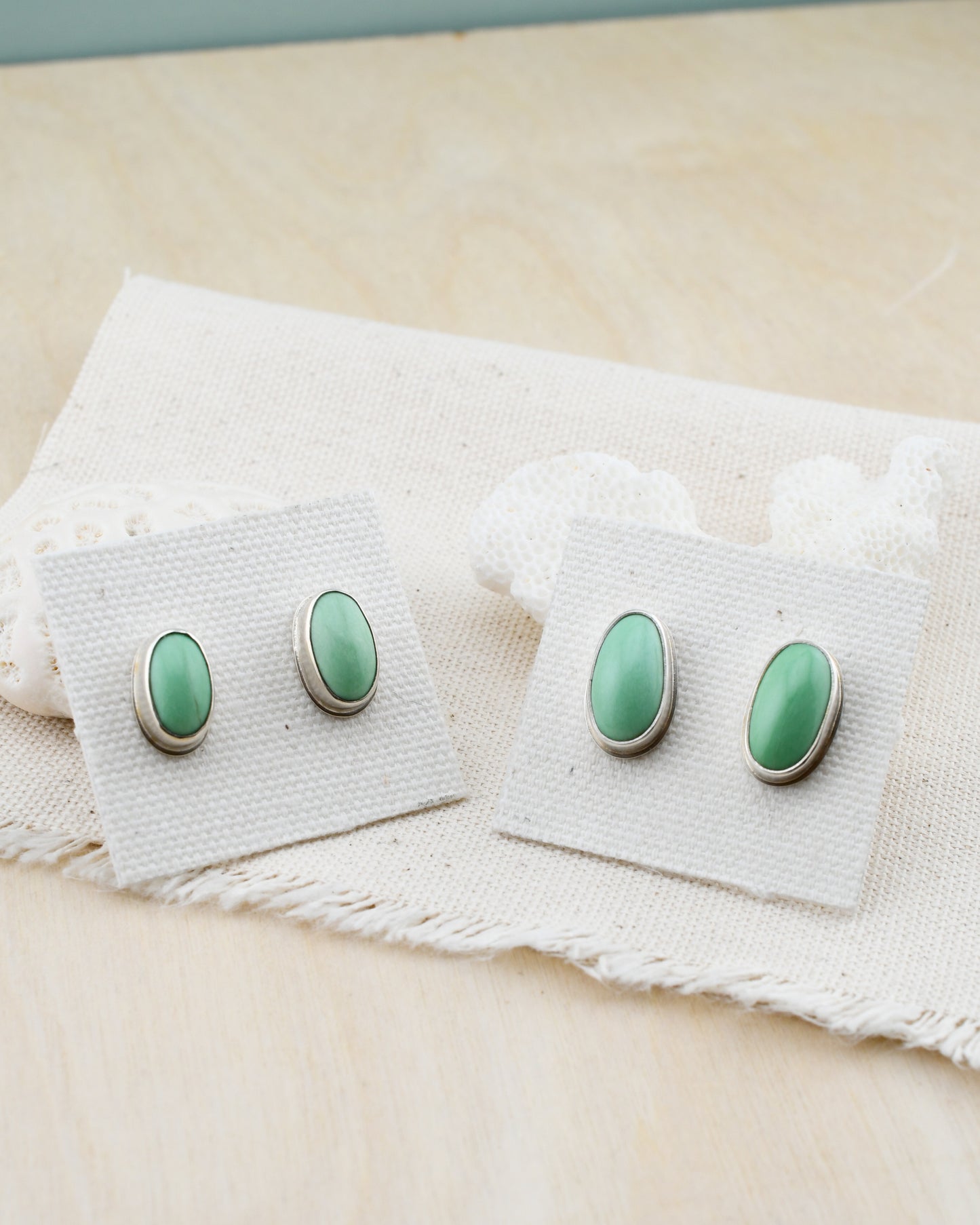2 pairs of green variscite and silver post earrings on linen cards and white coral with a pale wood background