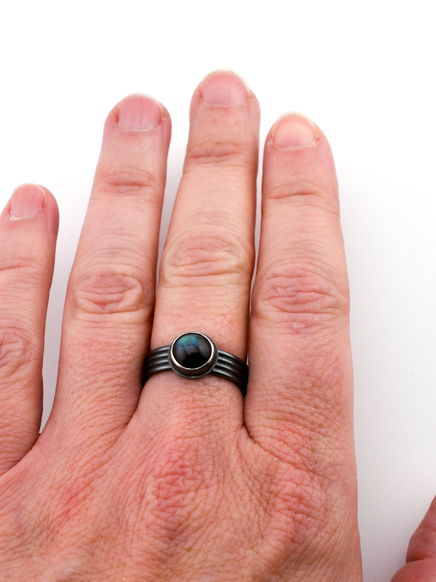 Hand wearing a black ring with a central gemstone on a white background