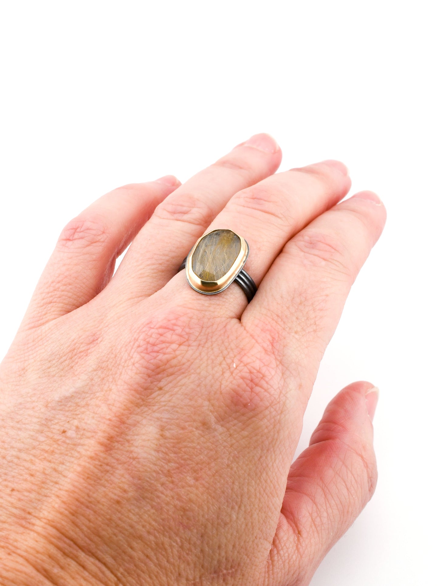 Black and gold rutilated quartz ring on a hand with a white background