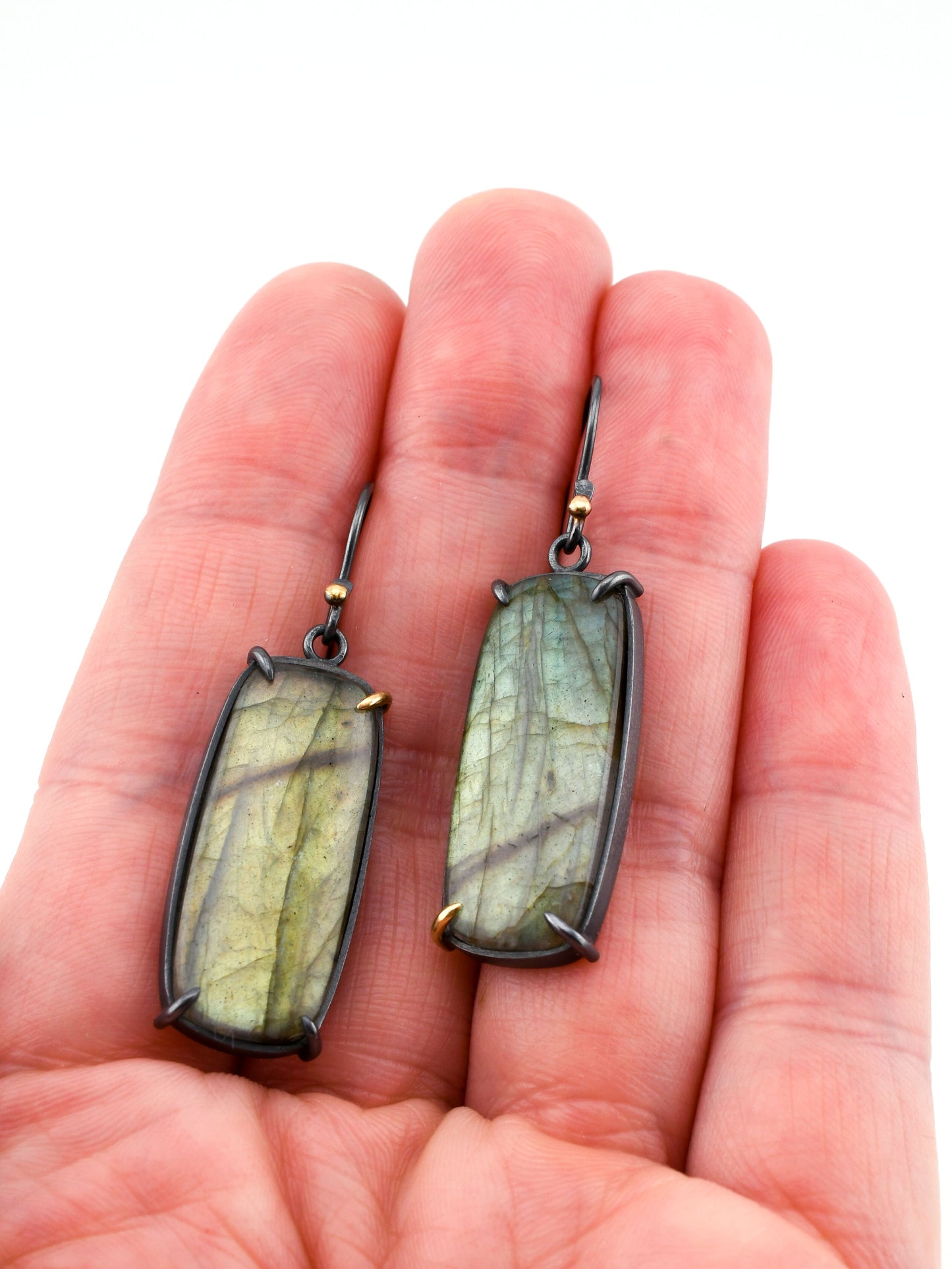 Pair of Labradorite earrings held in a hand on a white background
