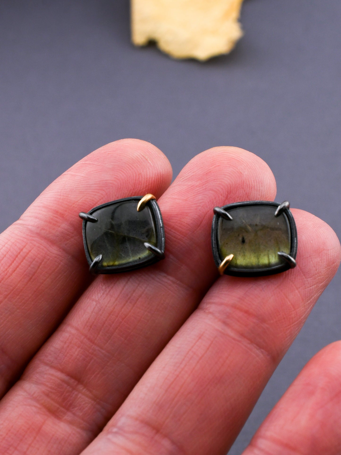 Pair of green gemstone earrings held between fingers against a dark background