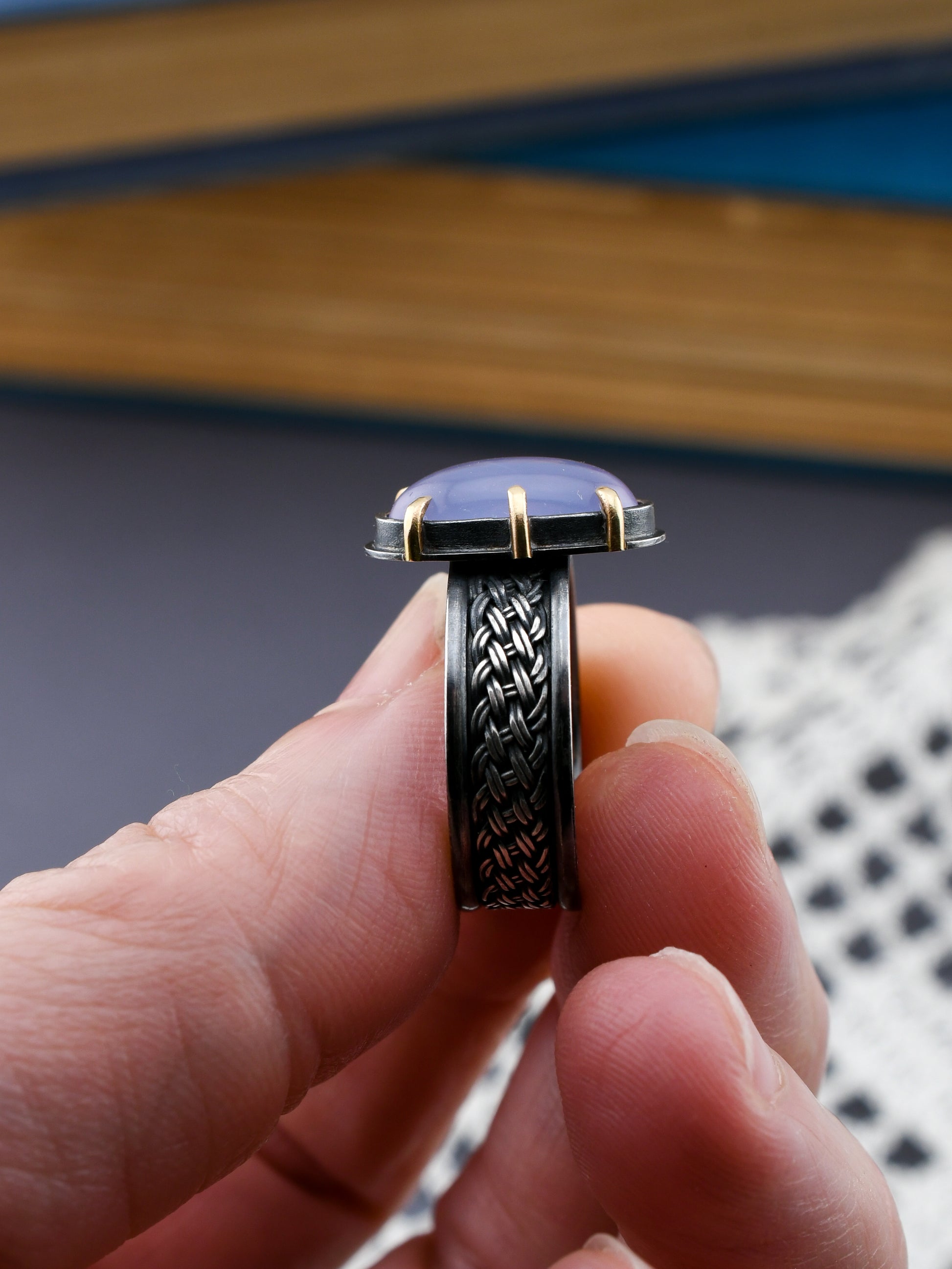 Hand holding a black silver woven ring with a blue stone against a blurred background