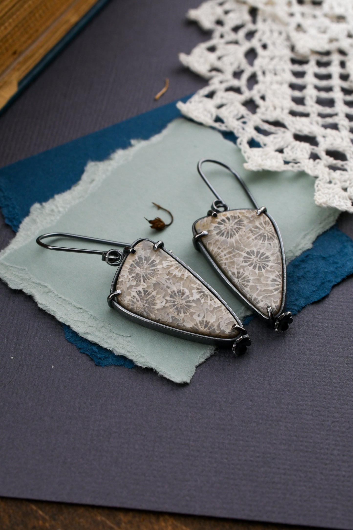 fossil coral earrings on a textured background with lace and a book