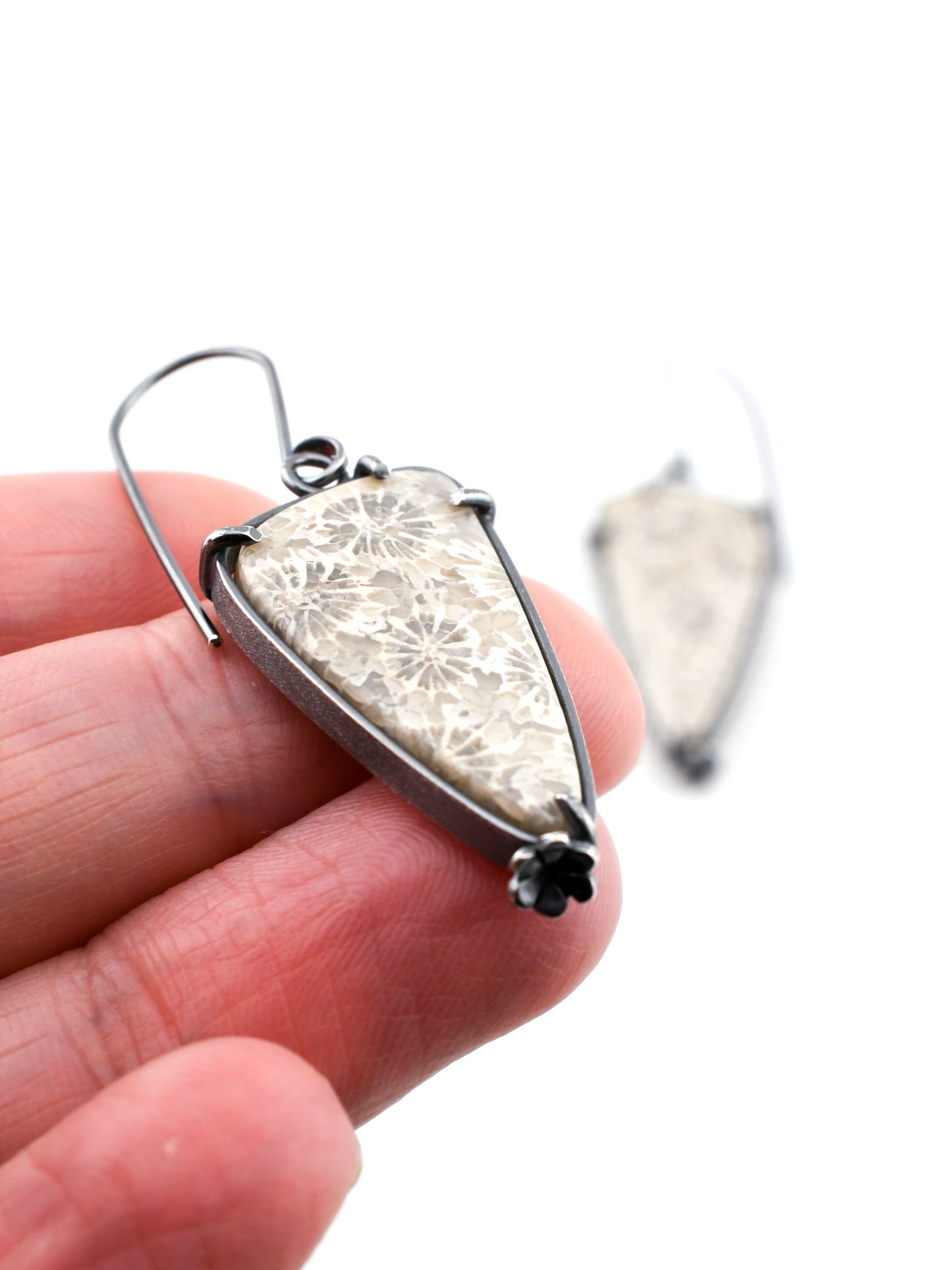 gray and white earring held between fingers on a white background