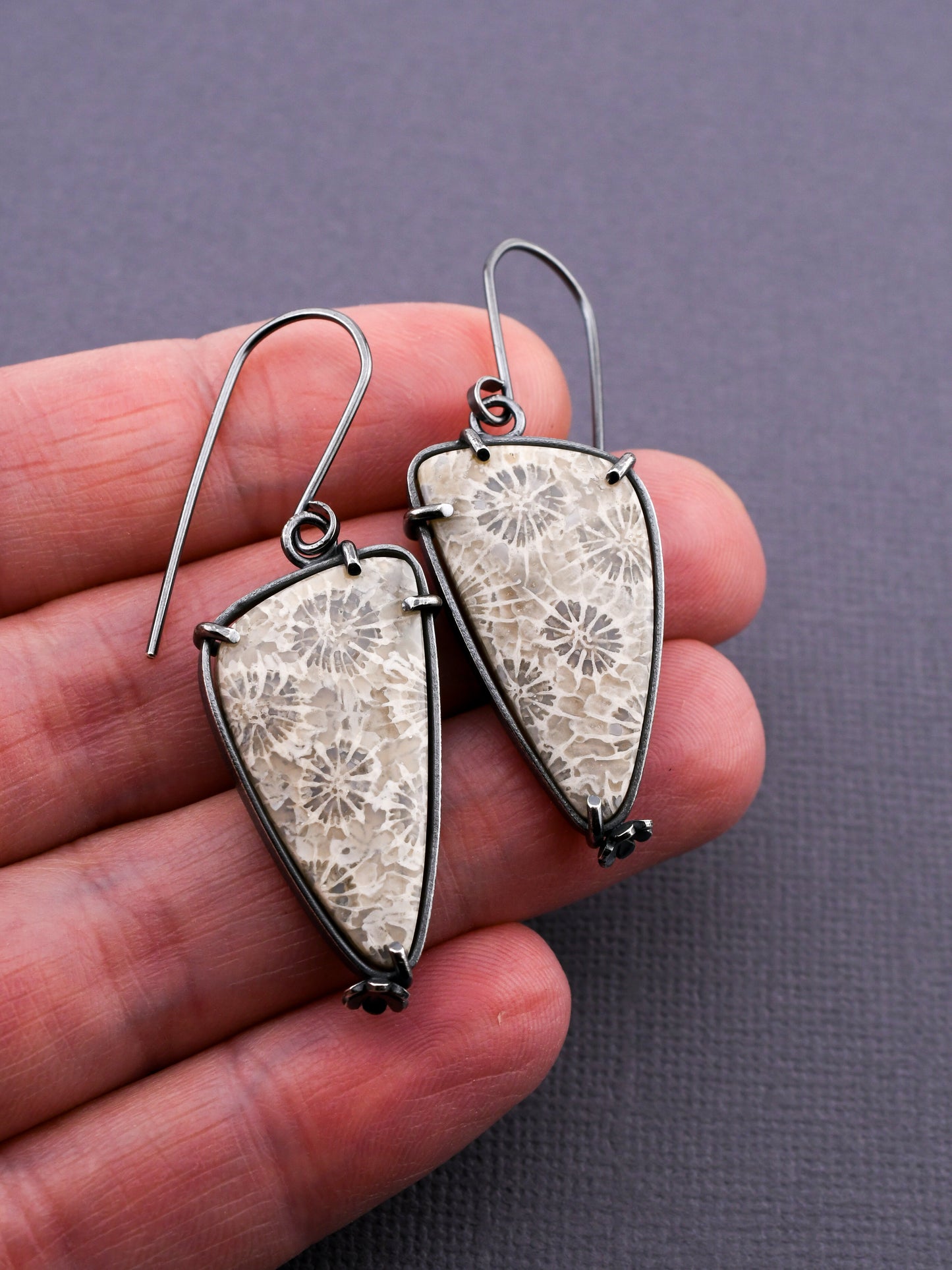 stone earrings held in a hand on a dark background