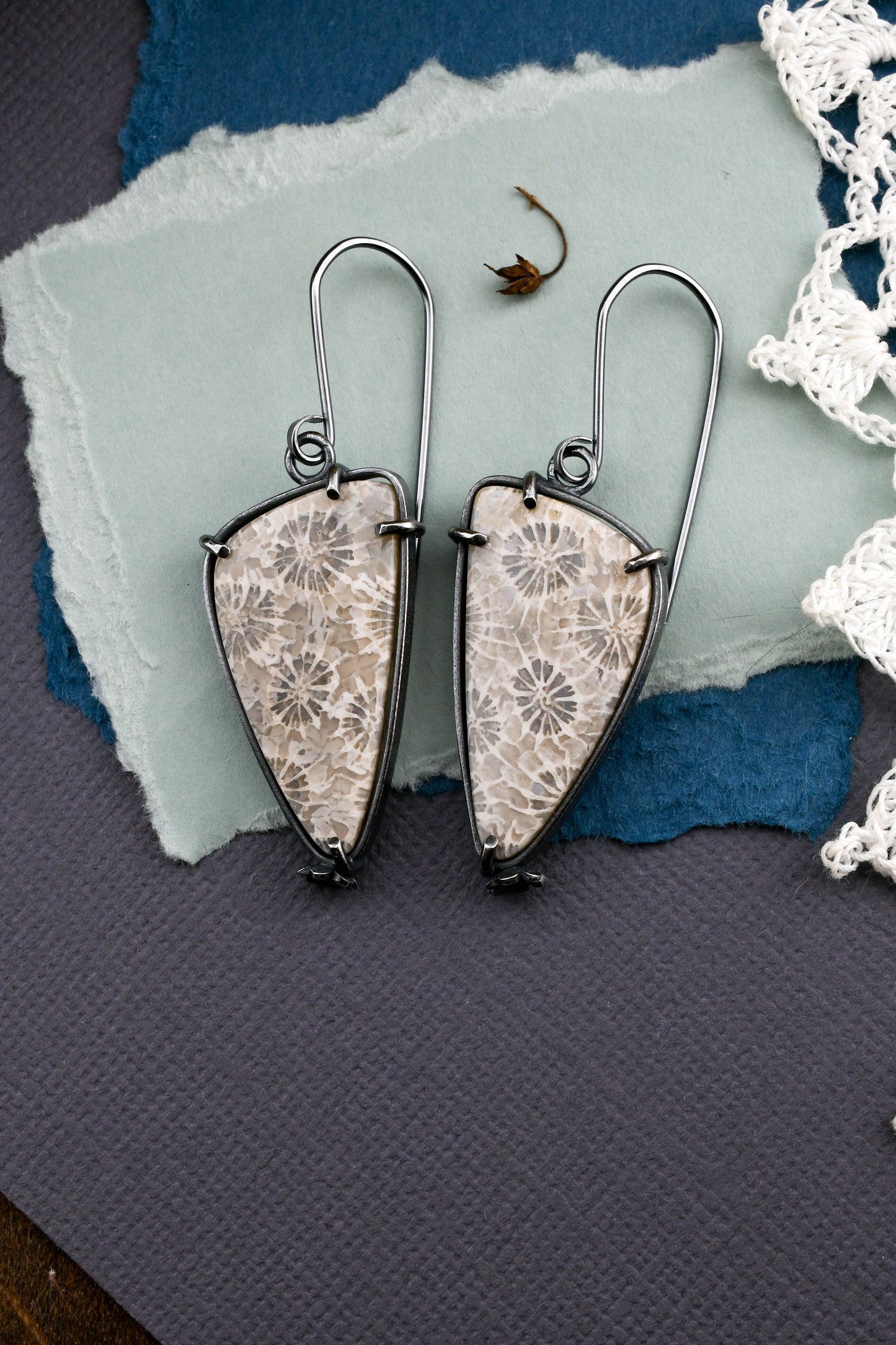 fossil coral earrings on textured blue paper with lace and a dried flower