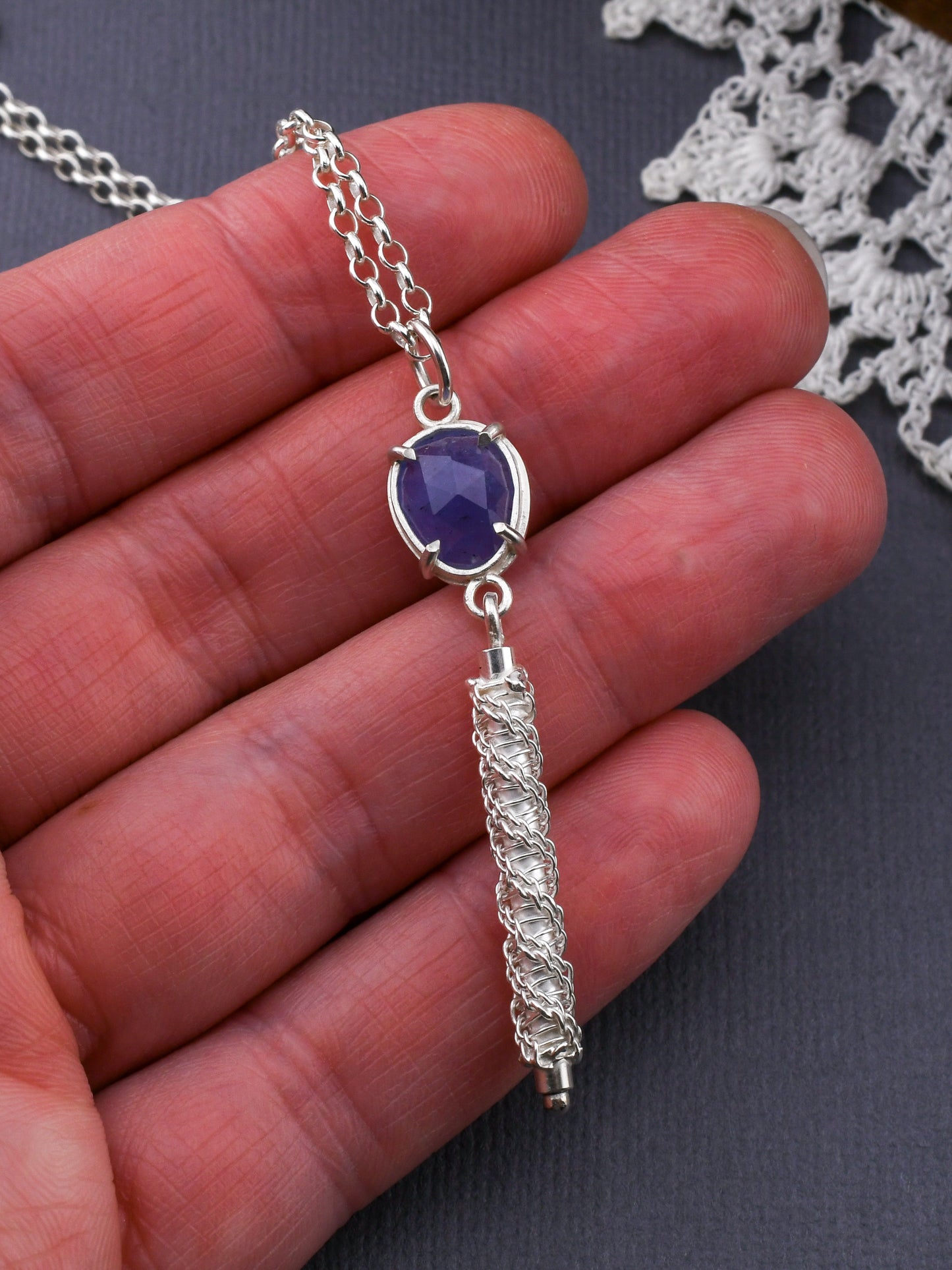 Silver necklace with a blue pendant held in a hand on a dark surface.