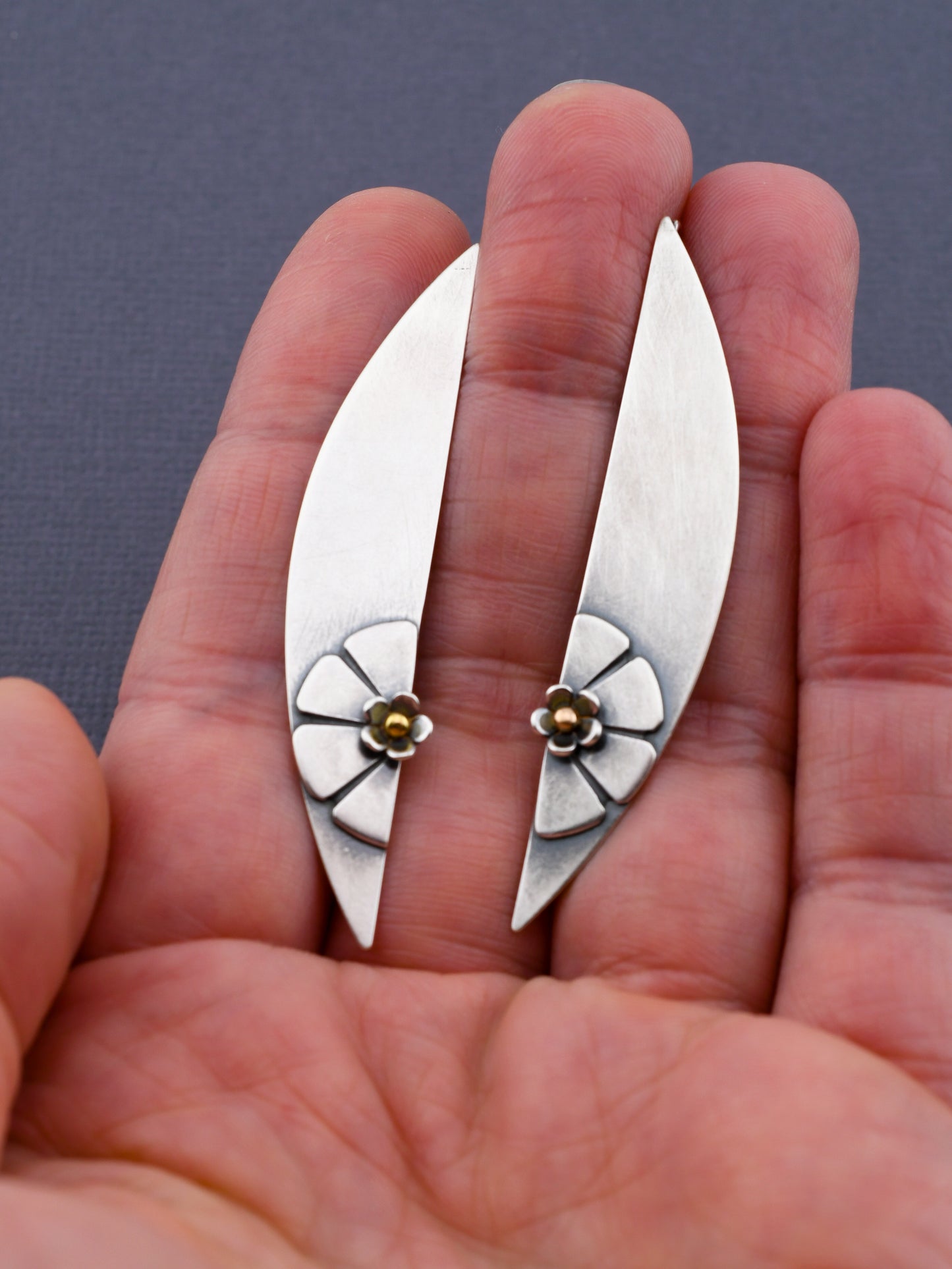 Silver earrings with floral designs held between fingers against a neutral background