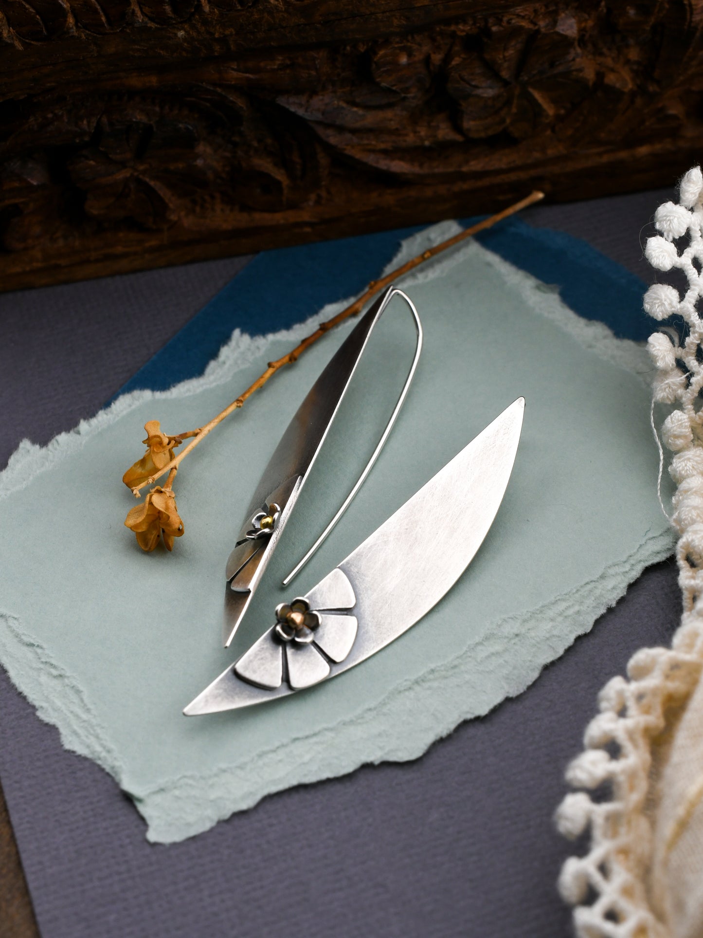 silver earrings on blue background with wooden box and lace in the background