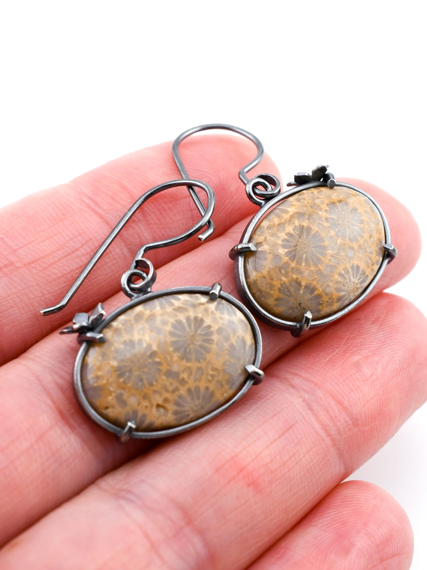 Fossilized coral earrings held in a hand against a white background
