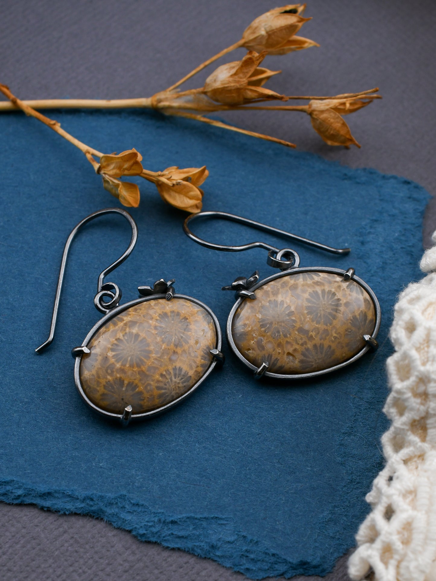 Pair of rustic stone earrings on a blue surface with dried flowers.