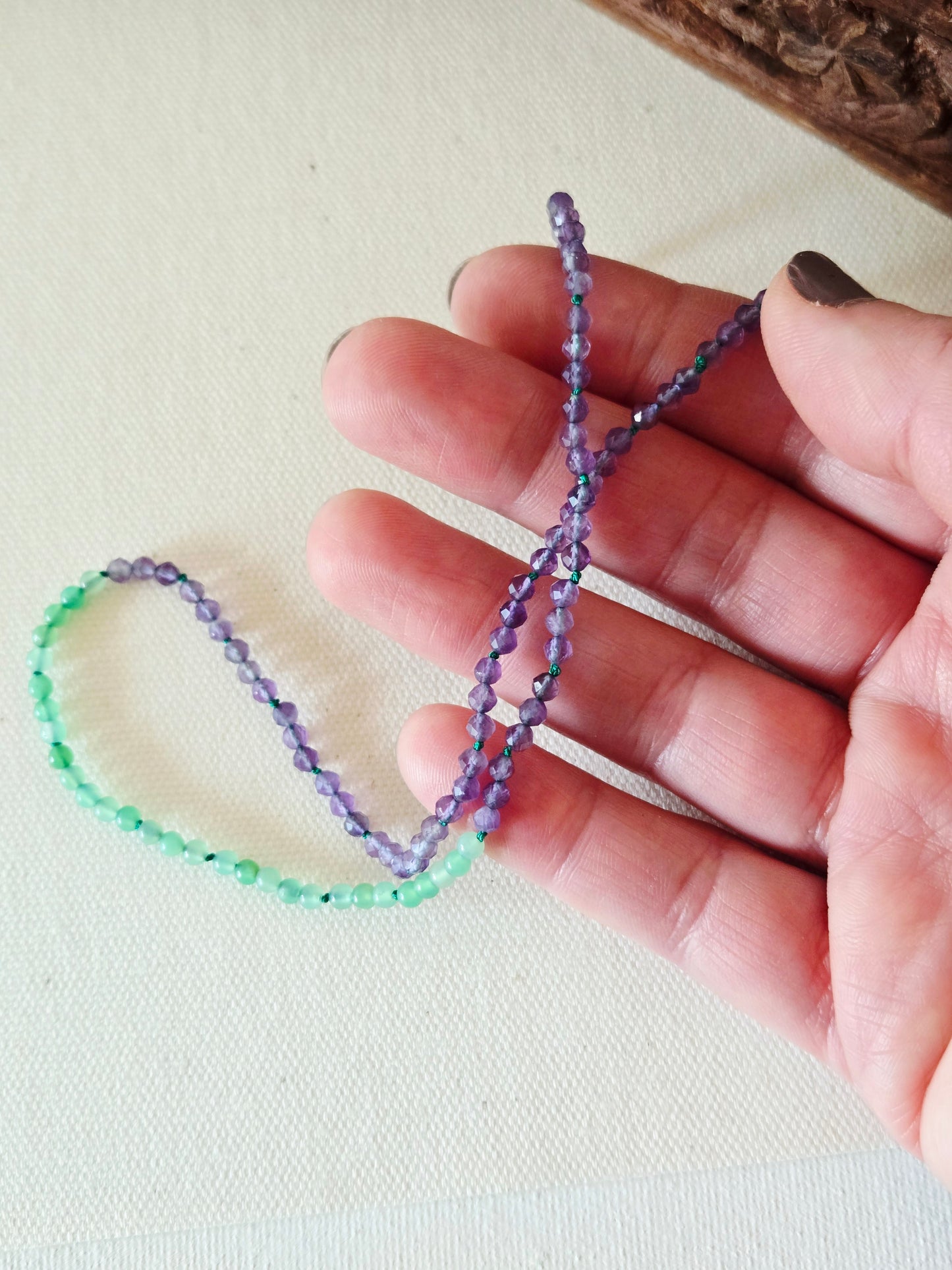 Hand holding a small, twisted necklace with beads on a light background