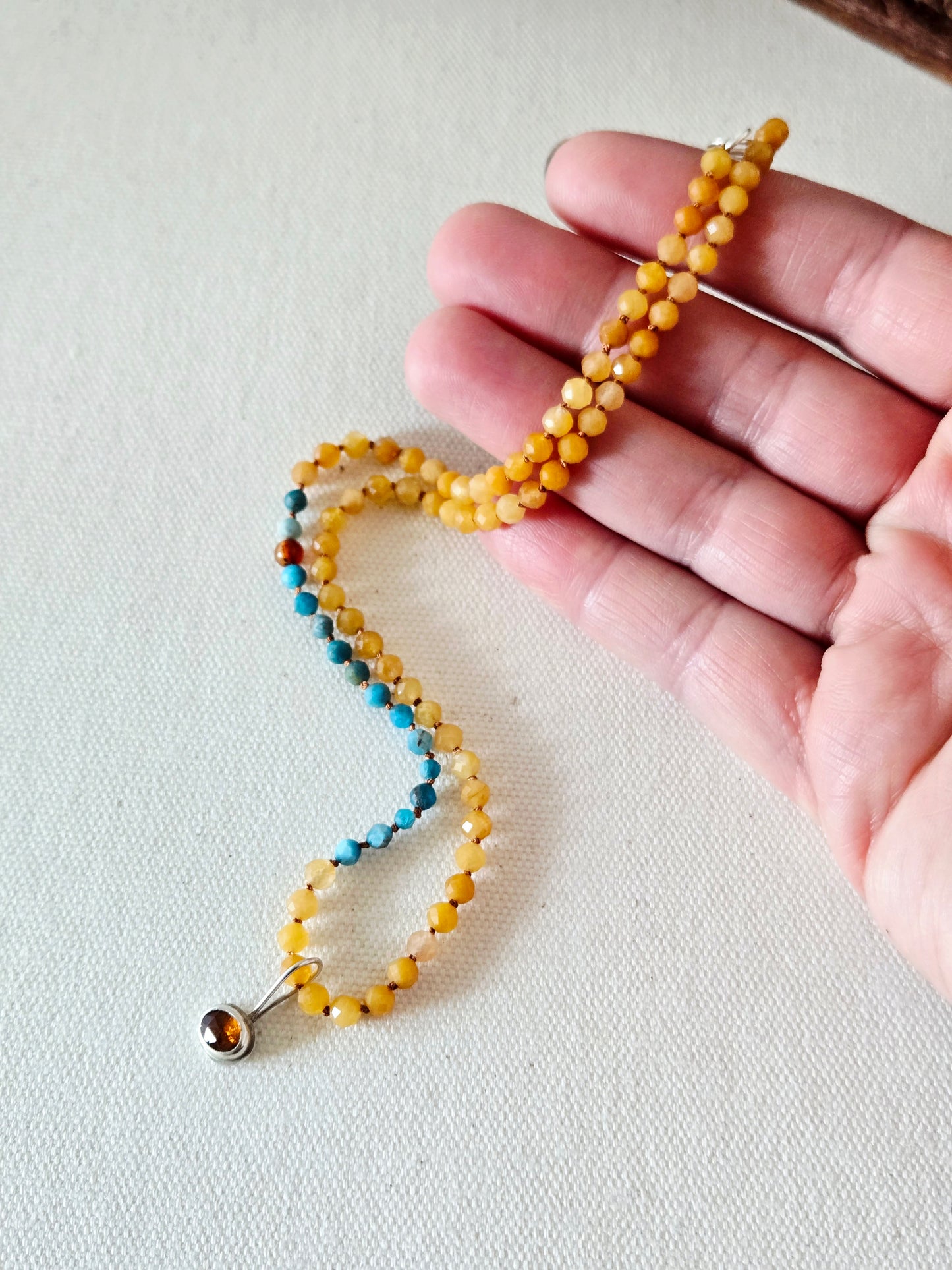 Hand holding a beaded necklace with yellow beads on a light background